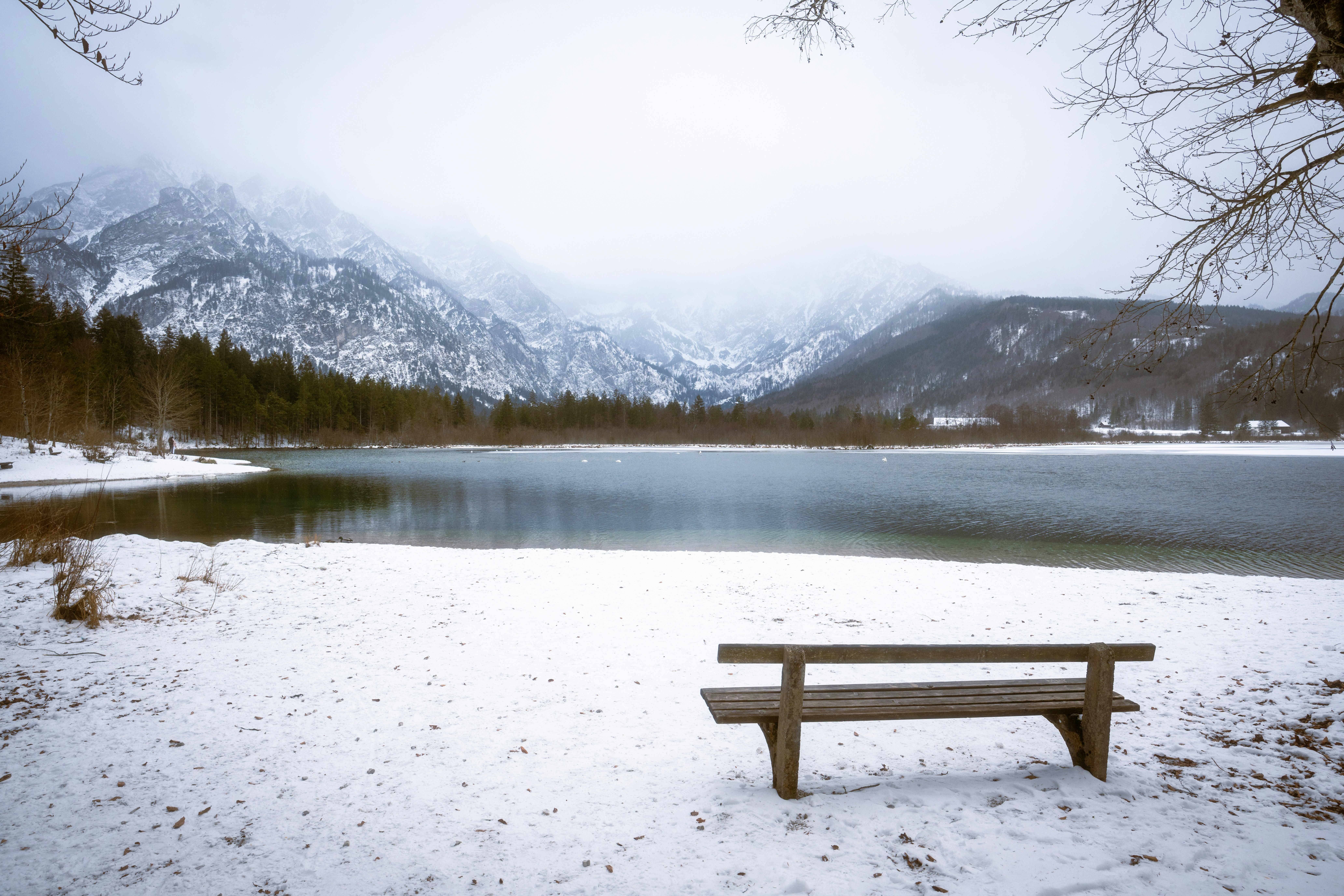 Un banco de madera junto a un lago helado con montañas nevadas.
