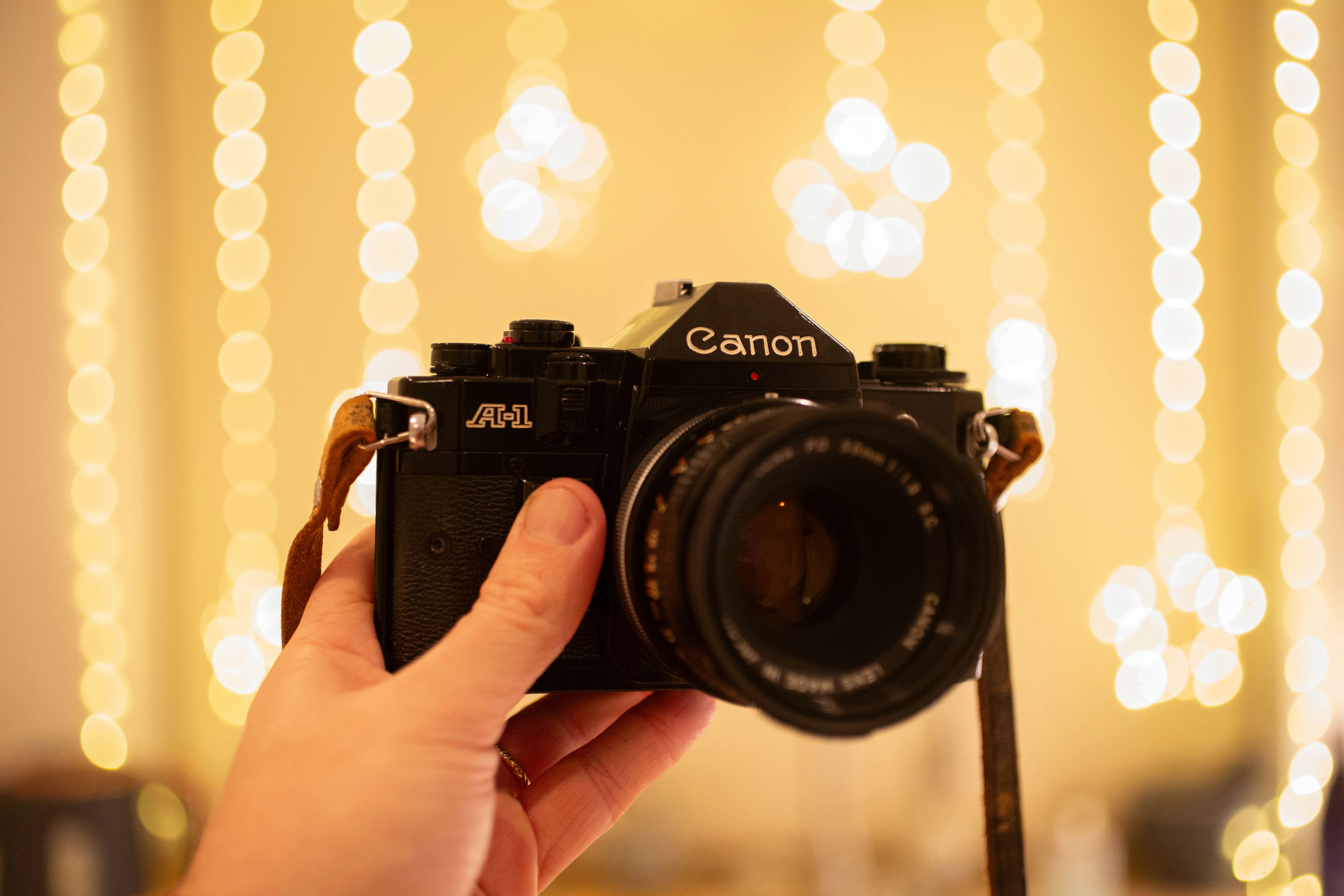 A hand holds an old canon camera with bokeh lights.