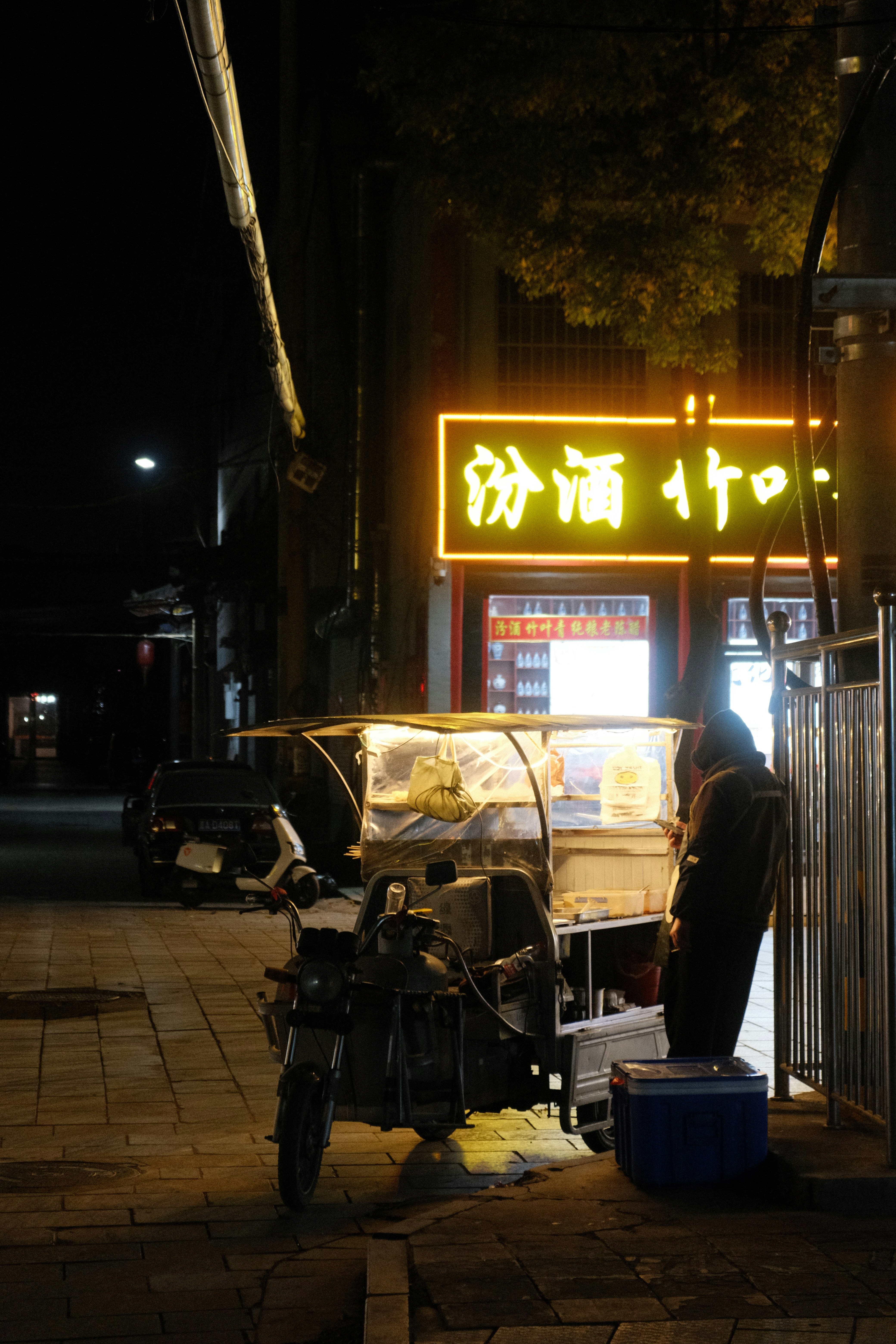 A person stands by a food cart at night.