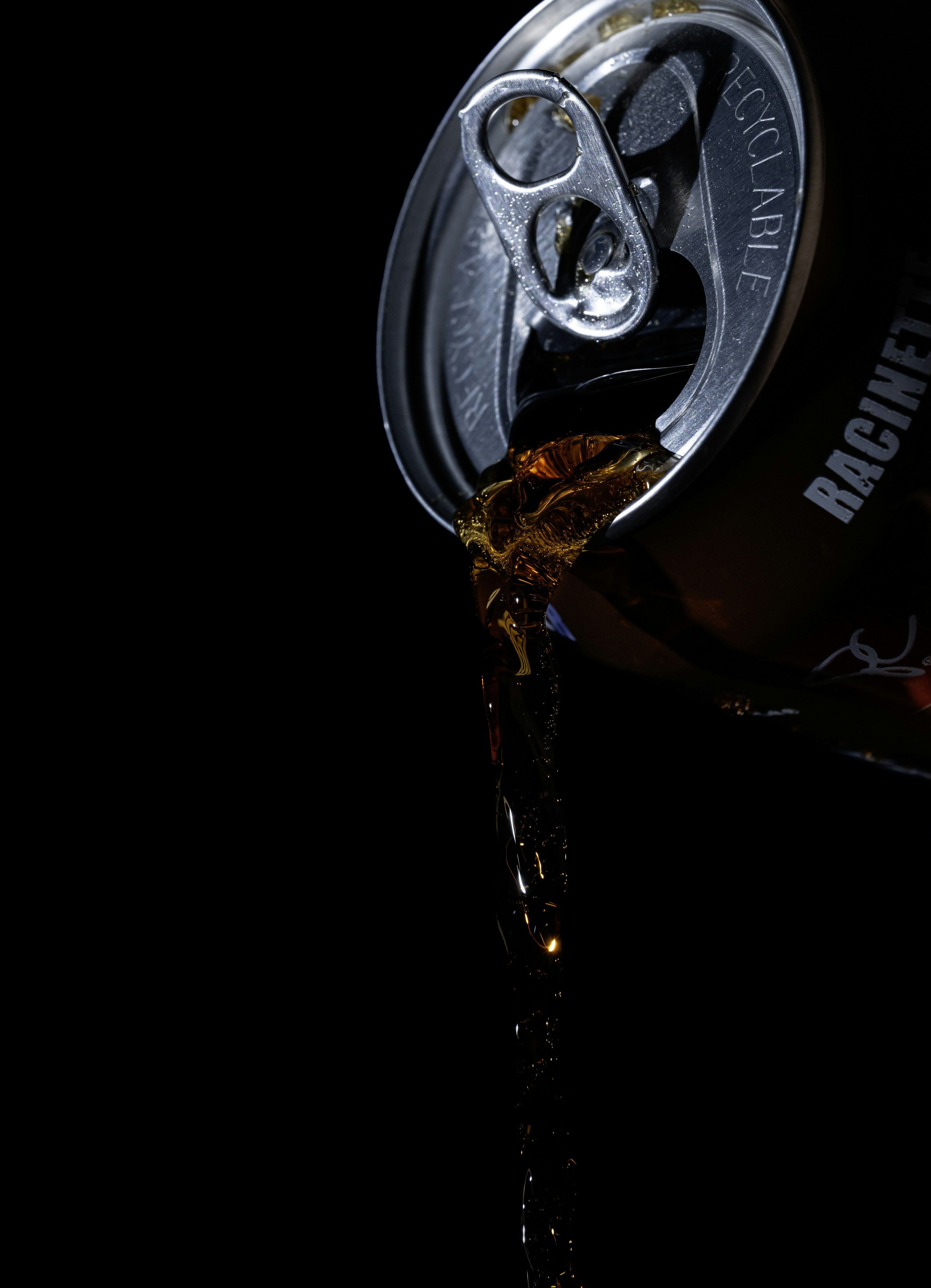 Dark soda being poured from an open can.
