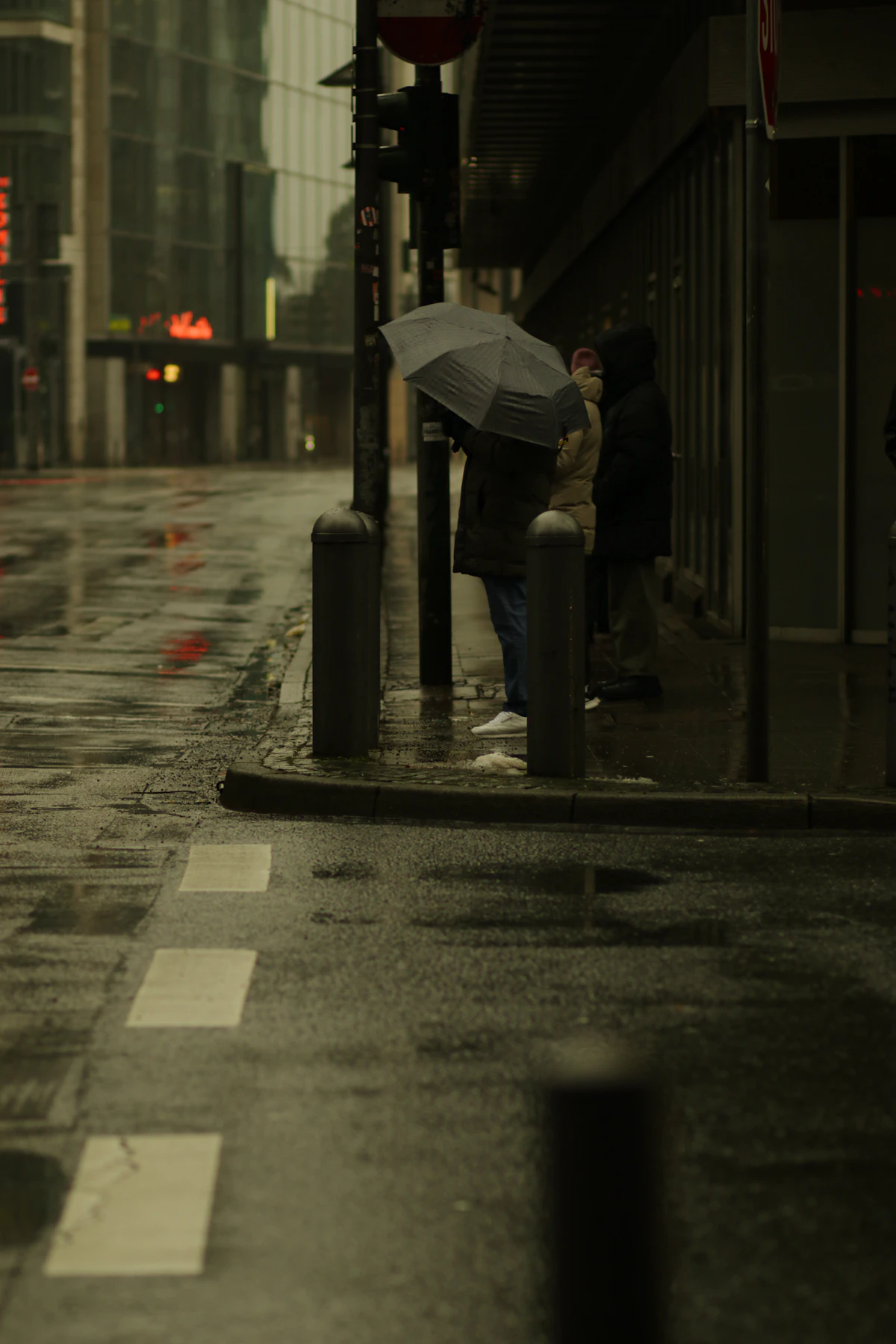 Menschen warten mit Regenschirmen an einer verregneten Straße