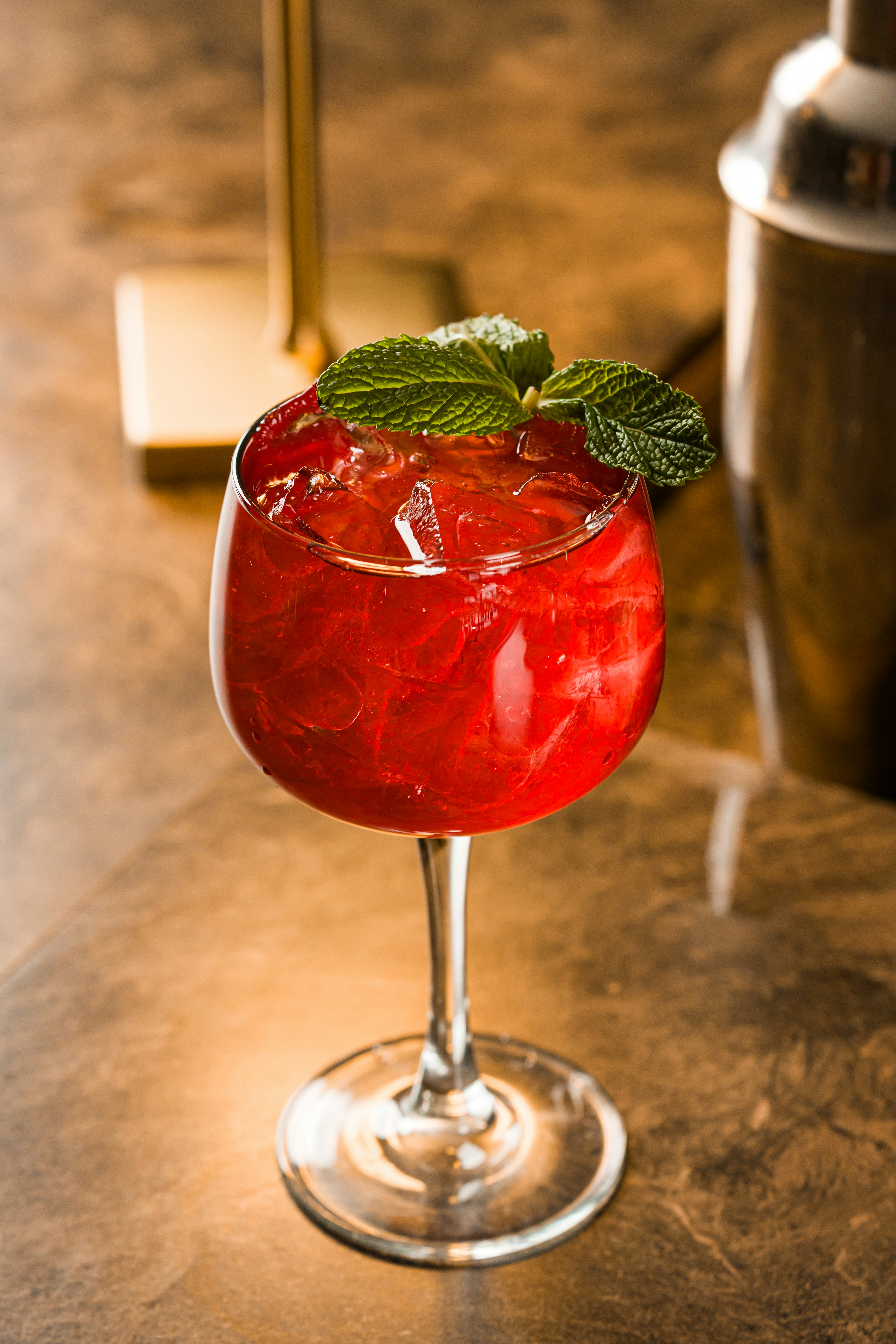 A refreshing red cocktail garnished with mint leaves.