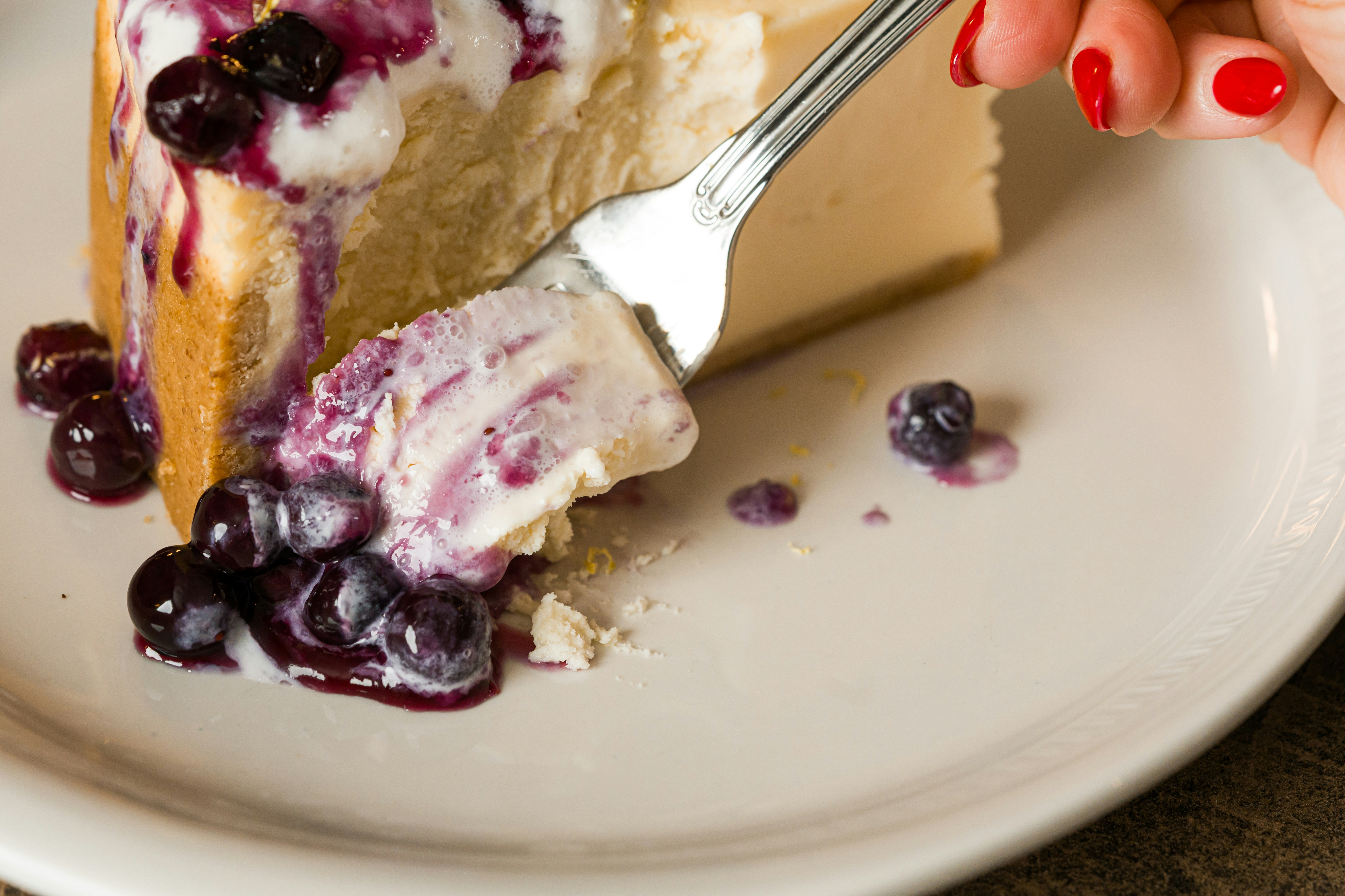 A fork takes a bite of cheesecake with blueberries.