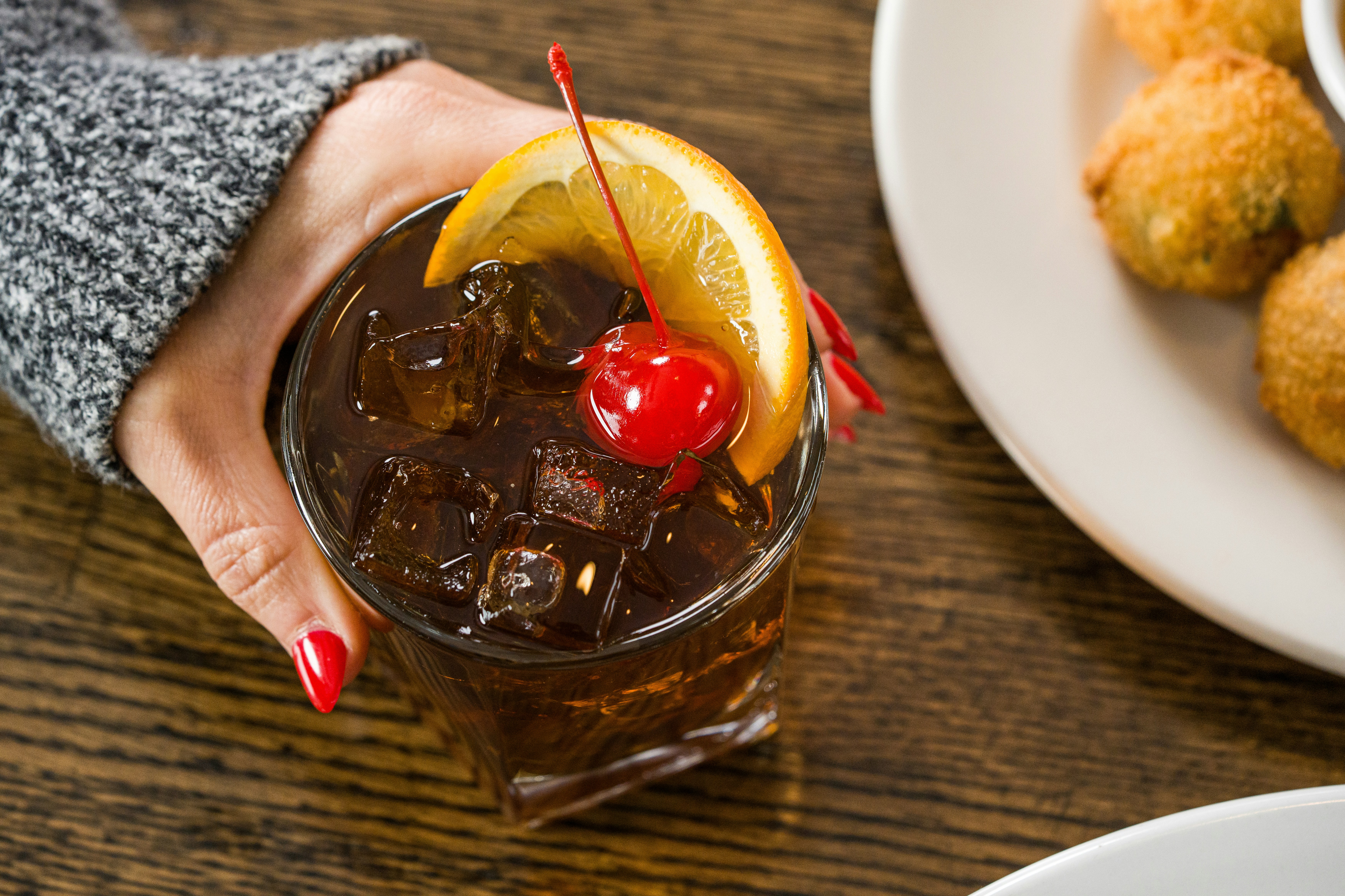 Hand holding a cocktail with orange slice and cherry