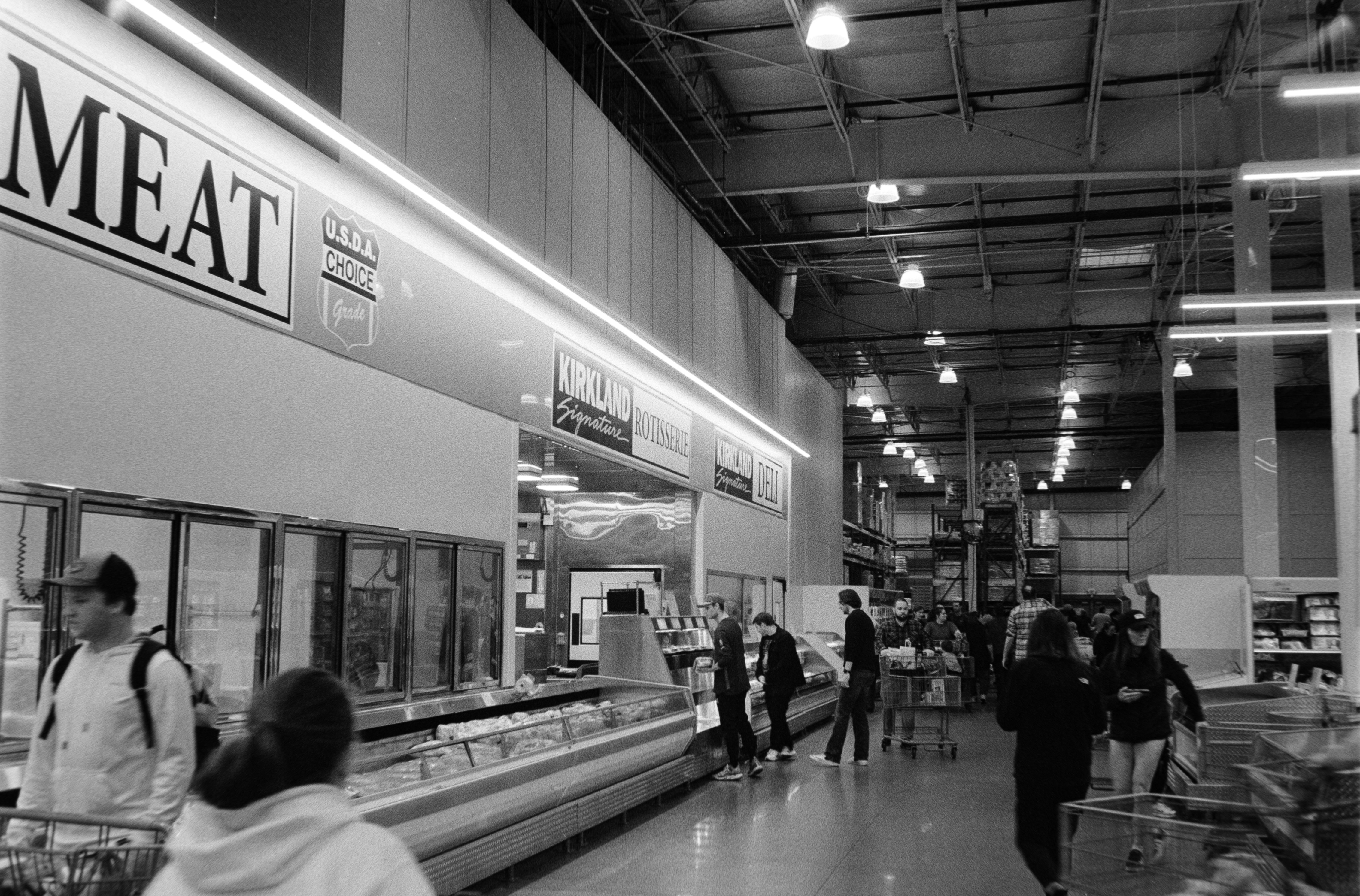 People shopping in a brightly lit grocery store meat section.