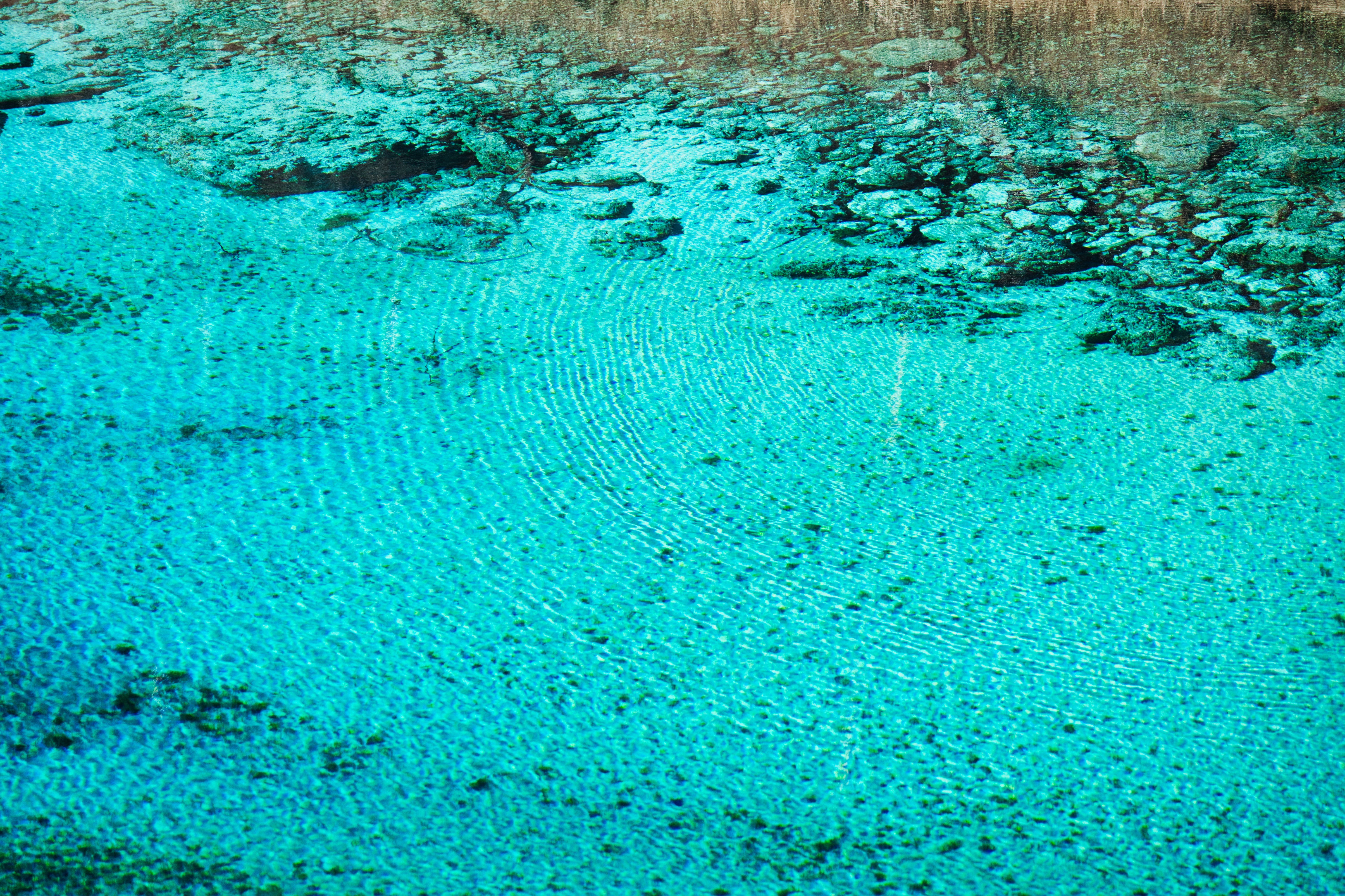 Crystal clear turquoise water with ripples and rocks.