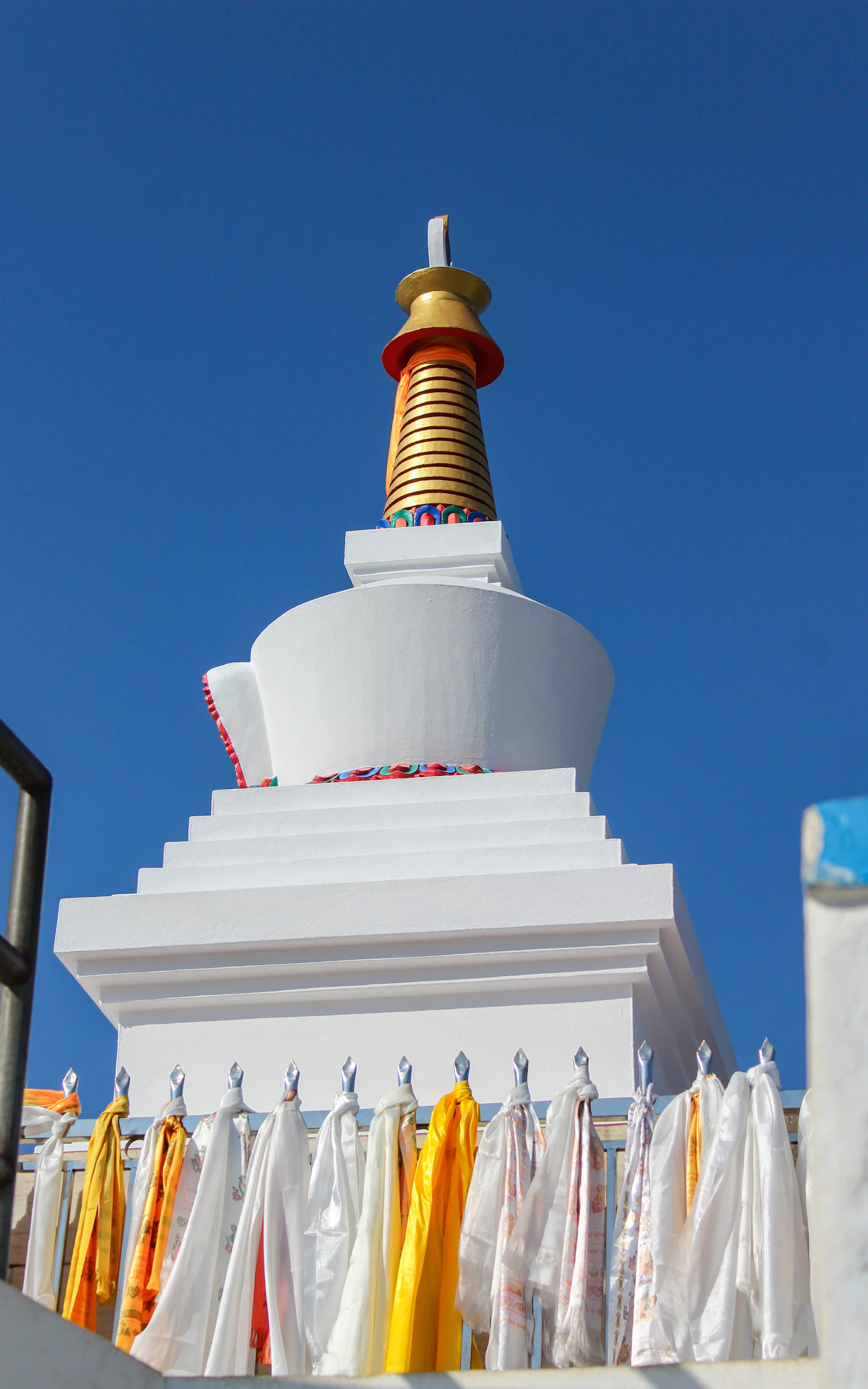 A white stupa with a golden spire and offering scarves against blue sky at Dhulikhel, Nepal