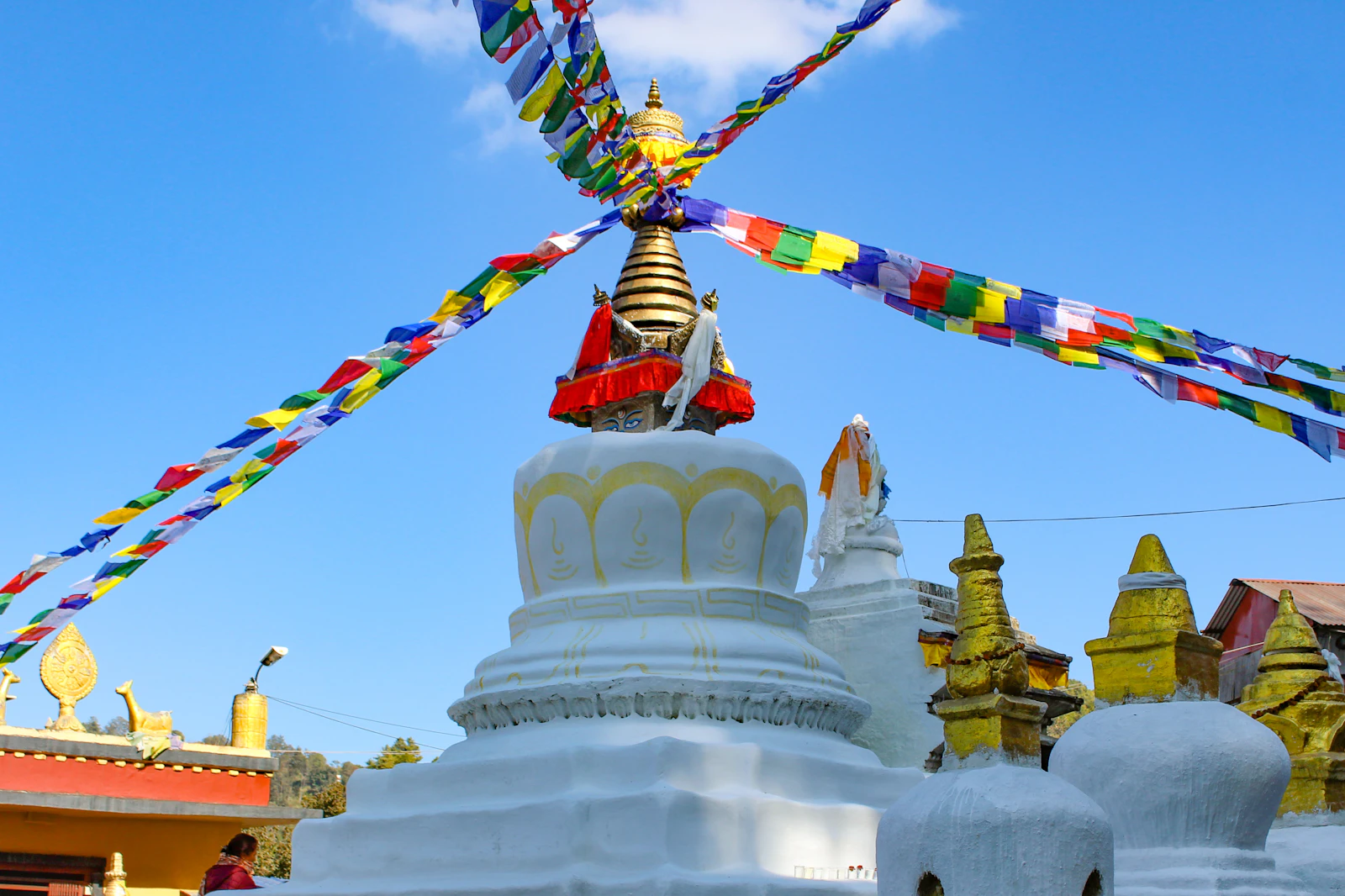 Prayer flags strung in a cross above the white Namo Buddha stupa near Dhulikhel, small gilded shrines around its base