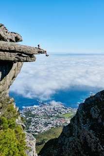 Person sitting on a cliff edge above clouds