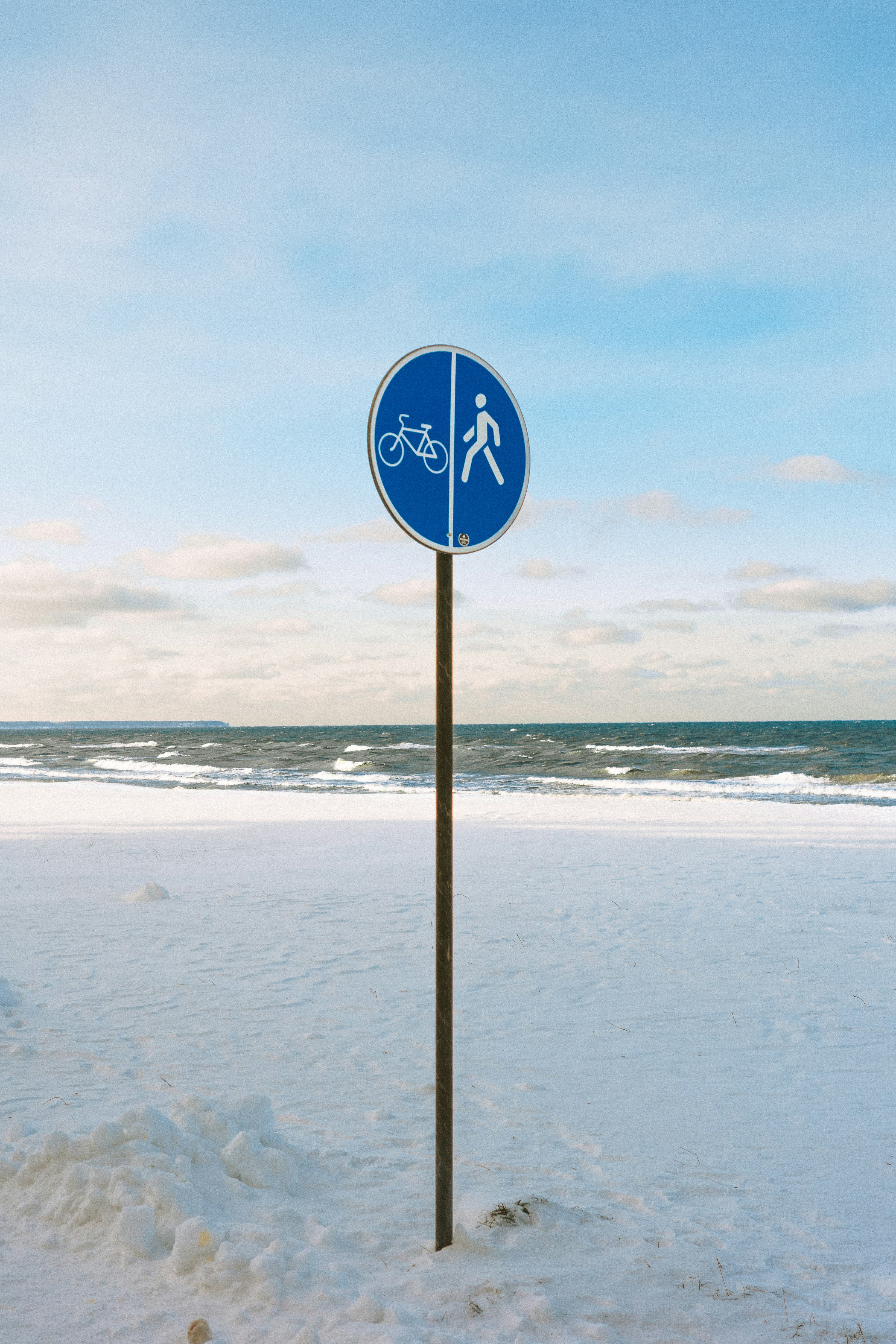 Bicycle and pedestrian path sign on snowy beach.