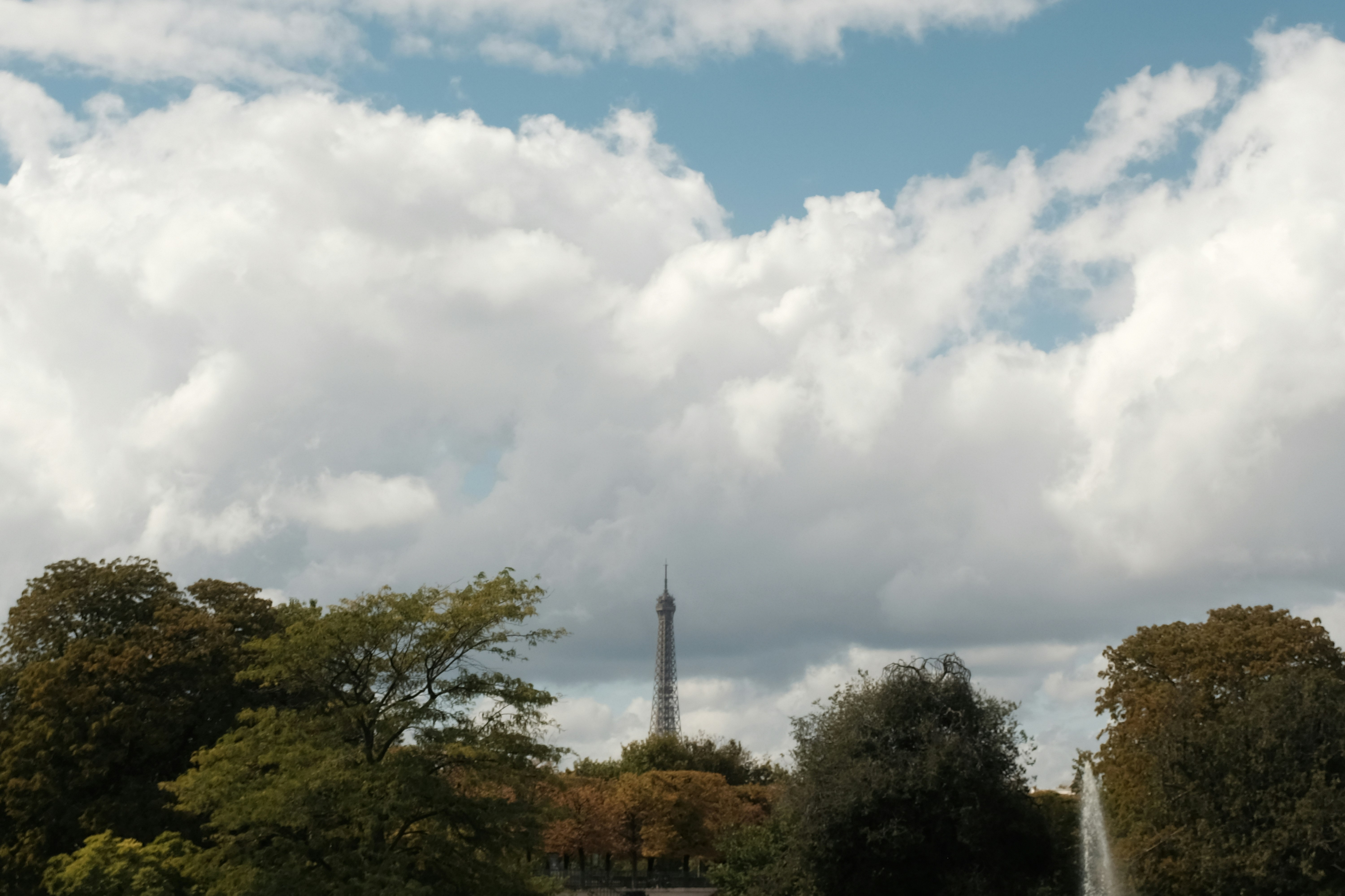 Tour Eiffel visible derrière les arbres sous un ciel nuageux