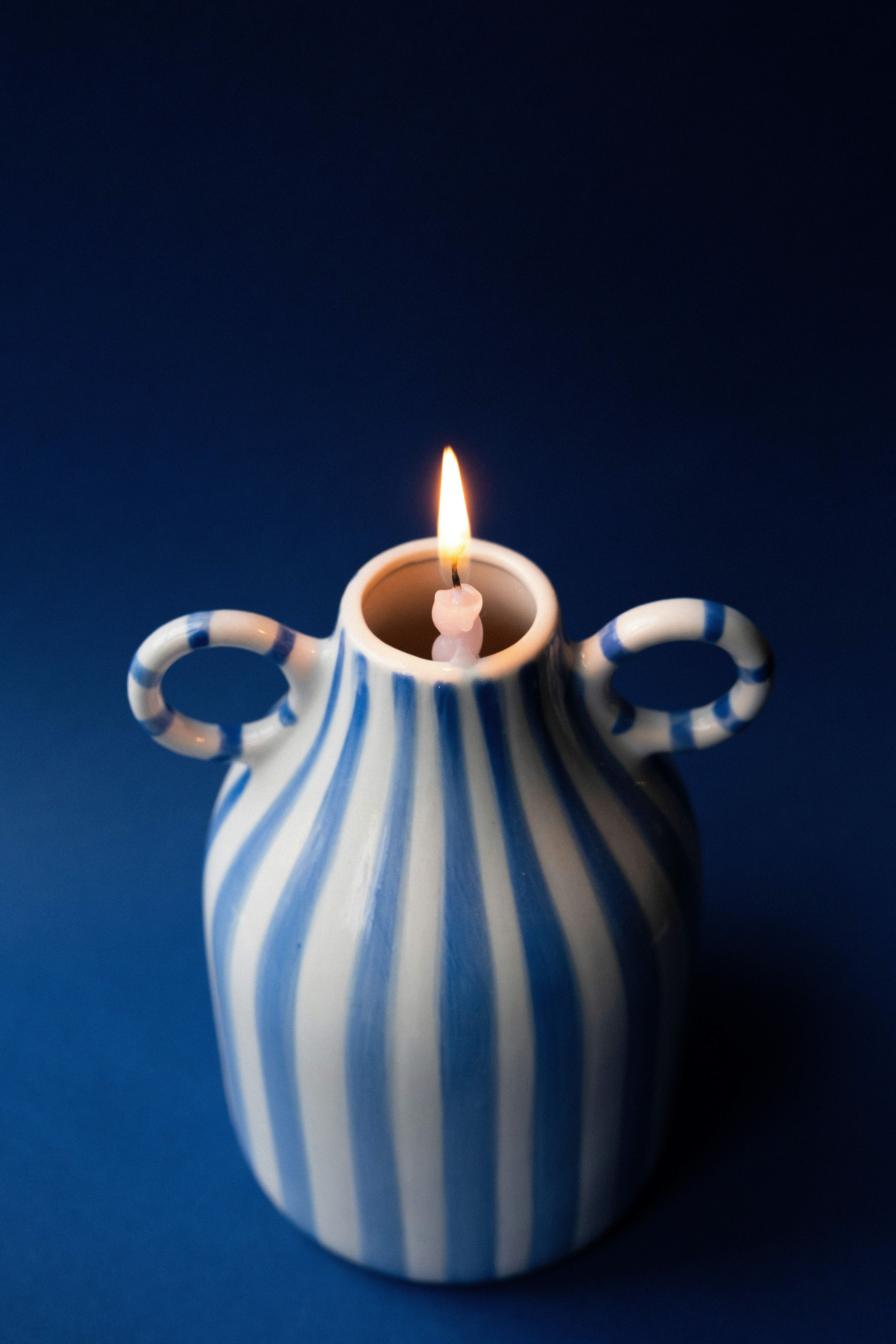 파란색과 흰색 줄무늬 꽃병에 켜진 촛불.