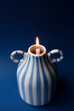 A lit candle in a blue and white striped vase.