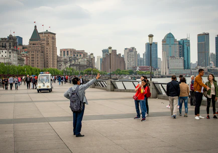 People taking photos along a waterfront with city skyline.