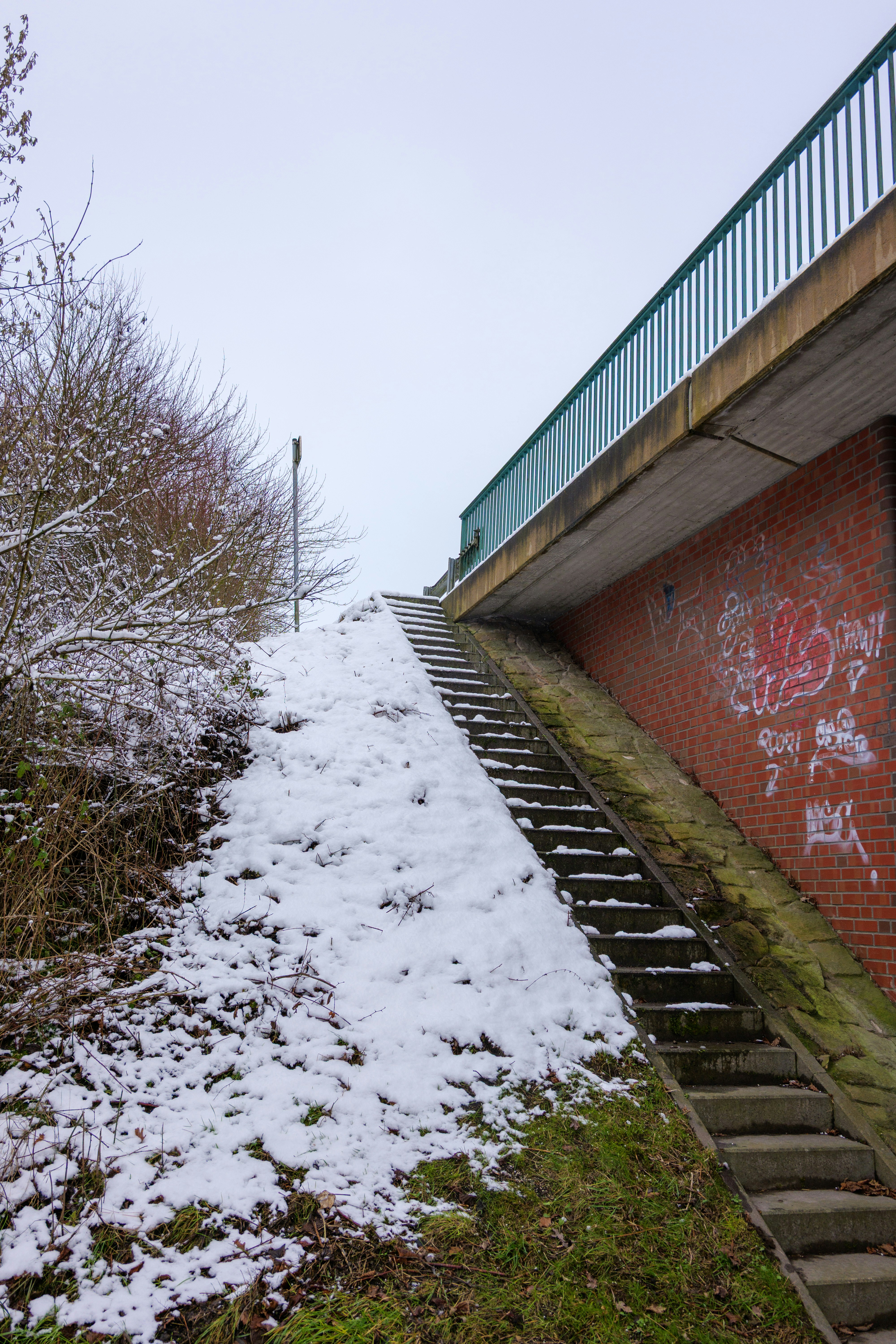 Snow-covered stairs ascend next to a brick wall.