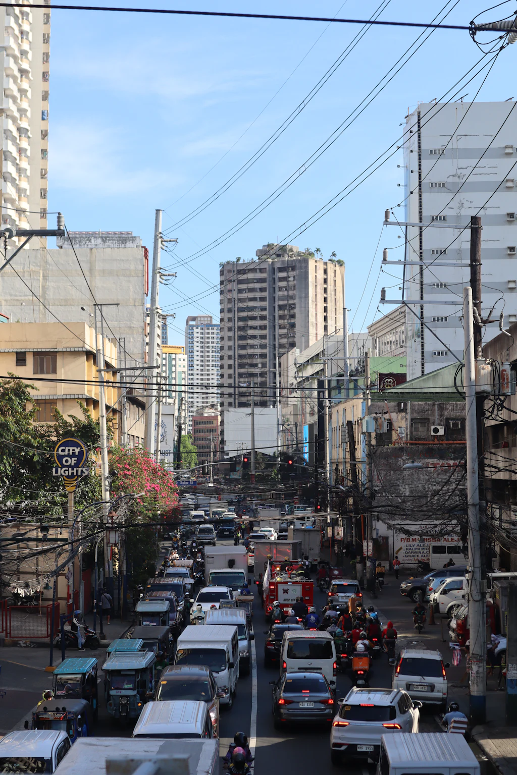 Dense Manila traffic, jeepneys and motorcycles beneath overhead cables between mid-rise buildings