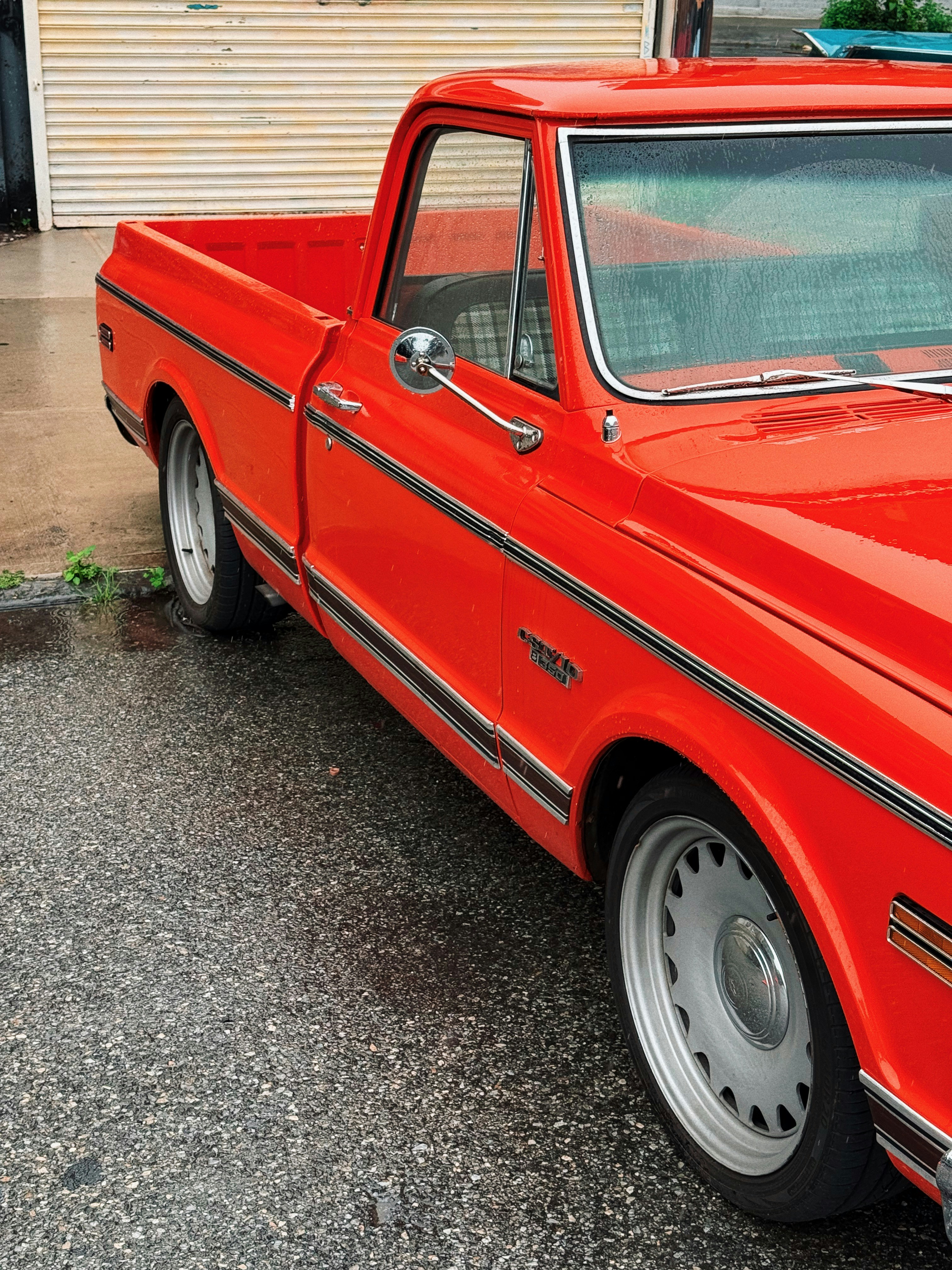 A bright red vintage pickup truck parked on wet pavement.