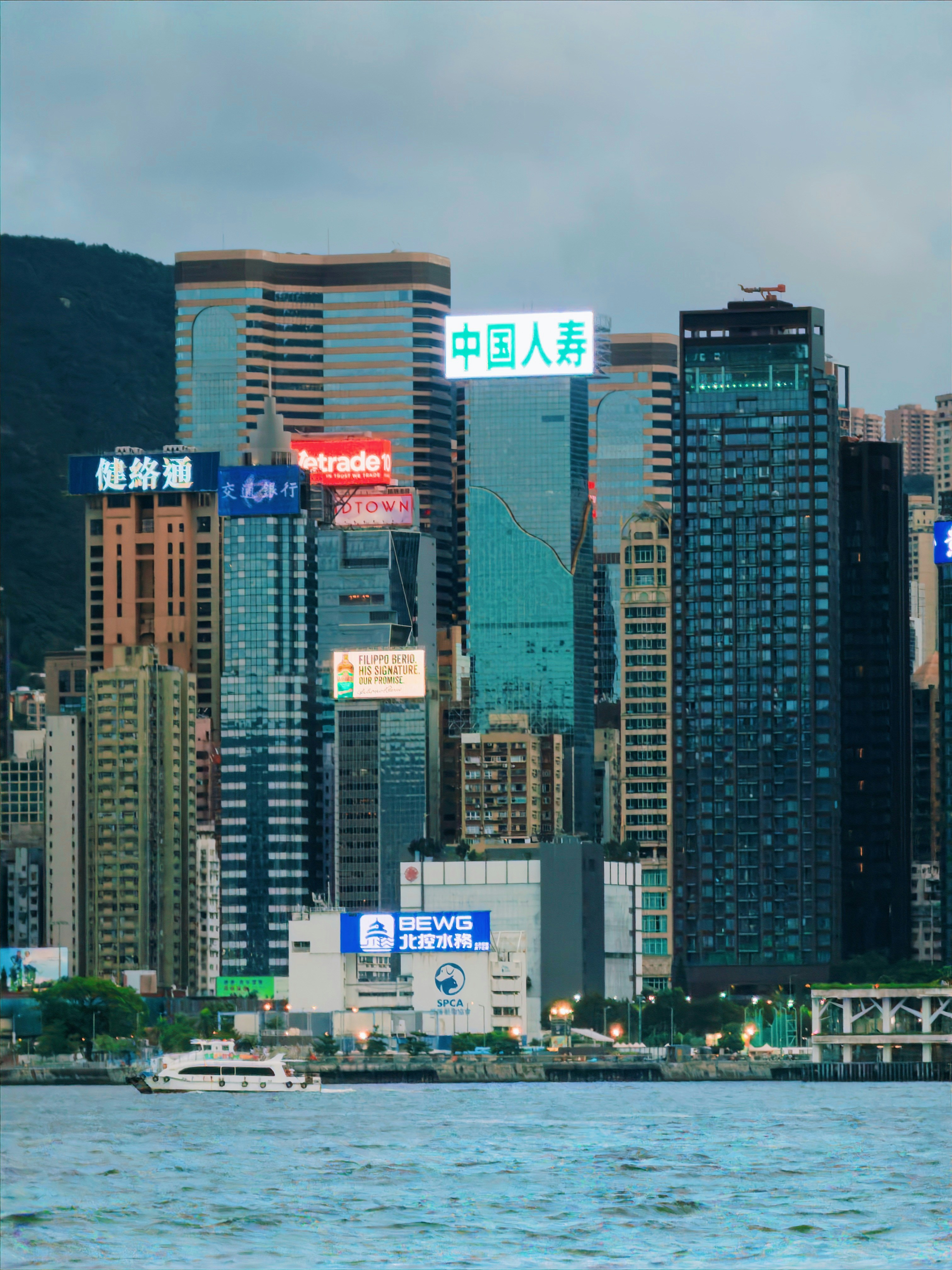 Modern skyscrapers with glowing signs by the water.