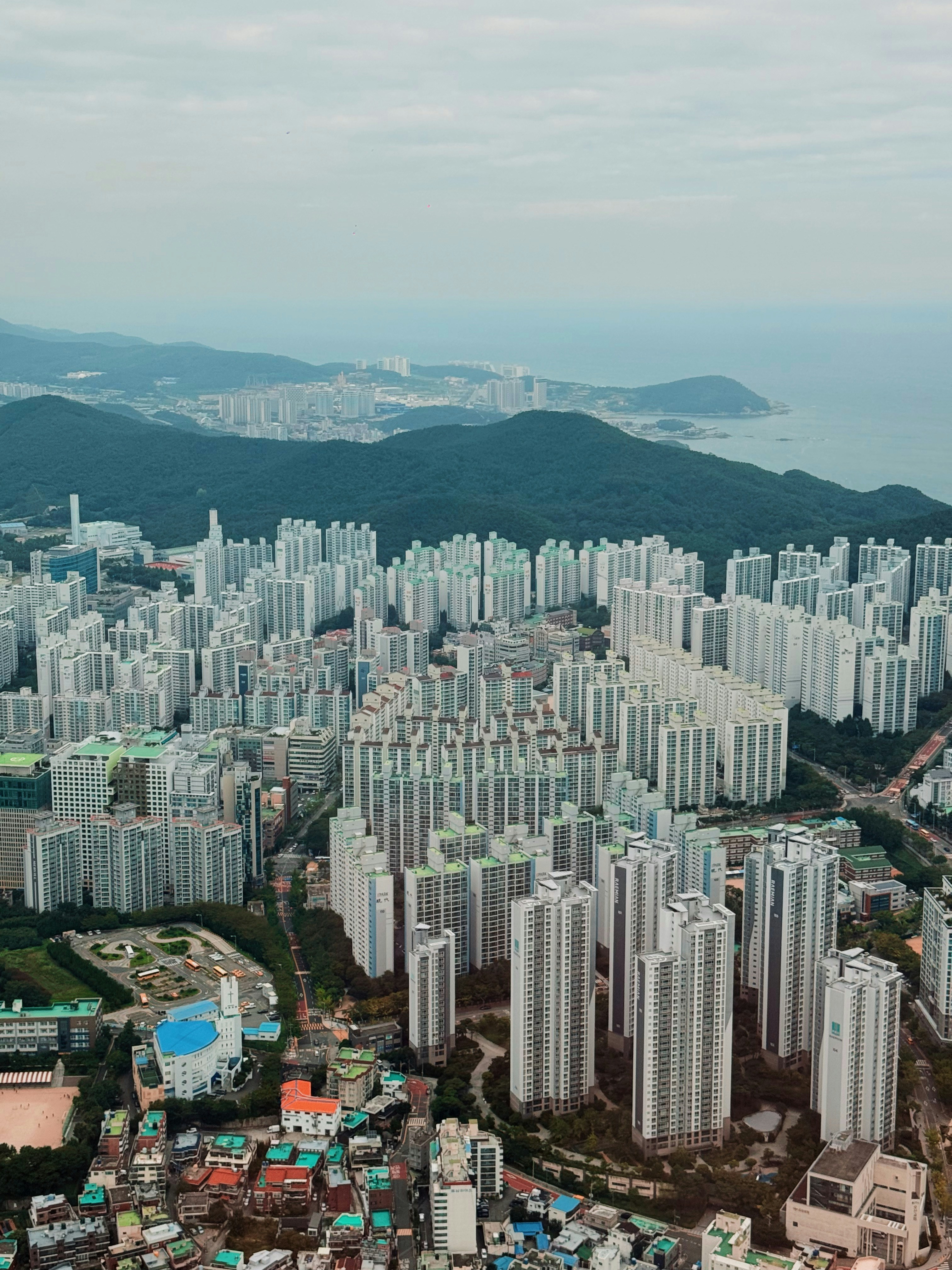 Dense apartment buildings stretch towards a hazy coastline.