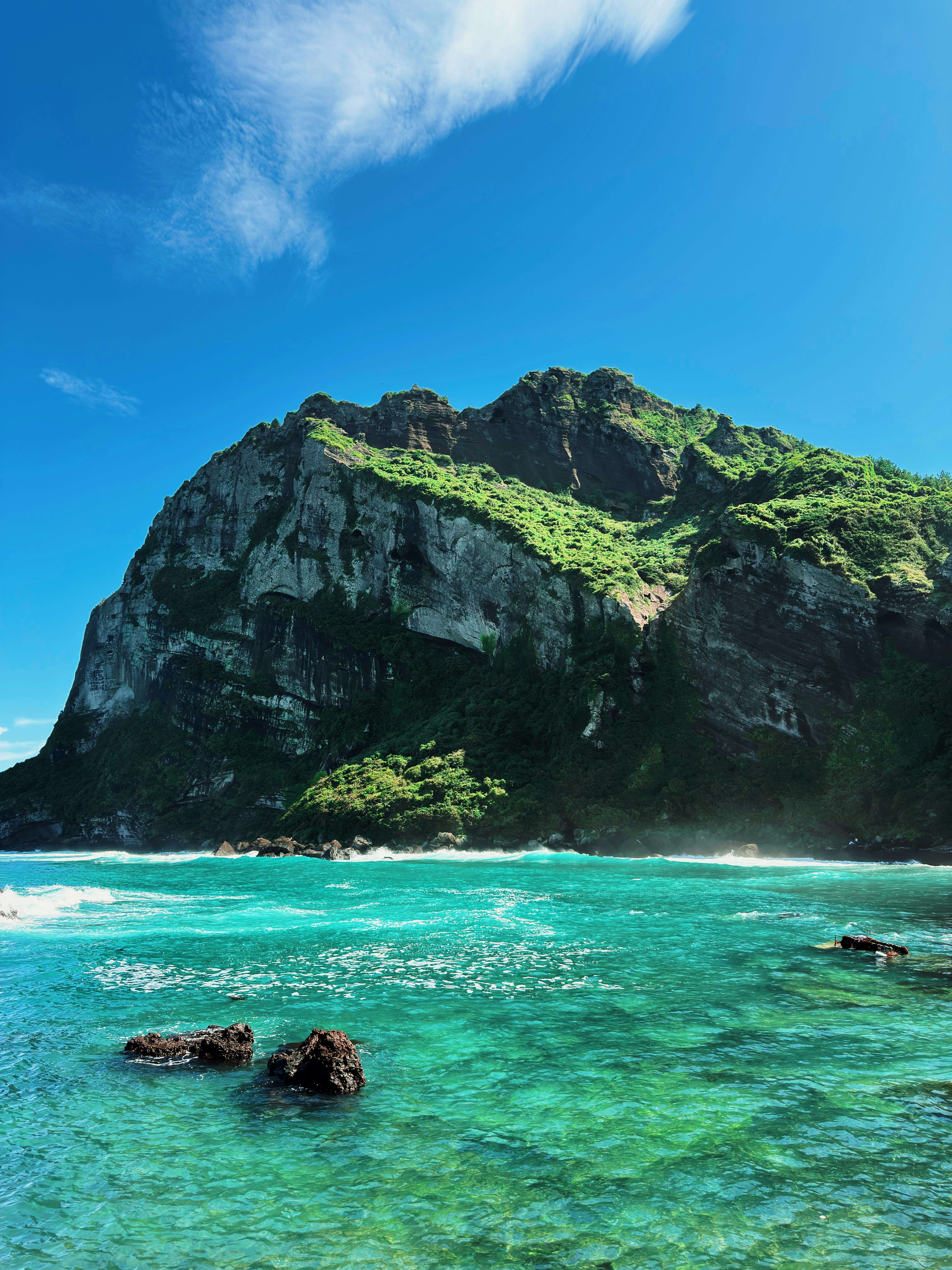 Lush green mountain meets turquoise ocean under a blue sky