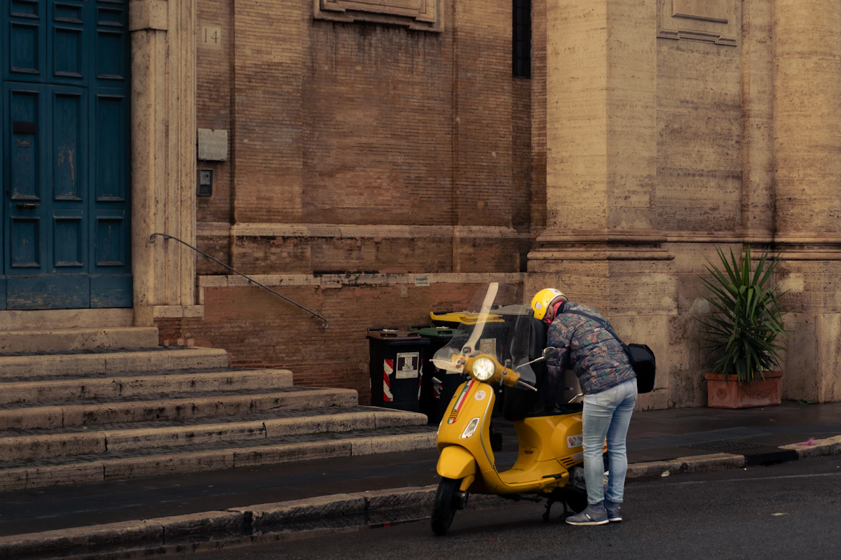 Vespa rider in yellow helmet standing beside his yellow Vespa scooter in Rome, Italy