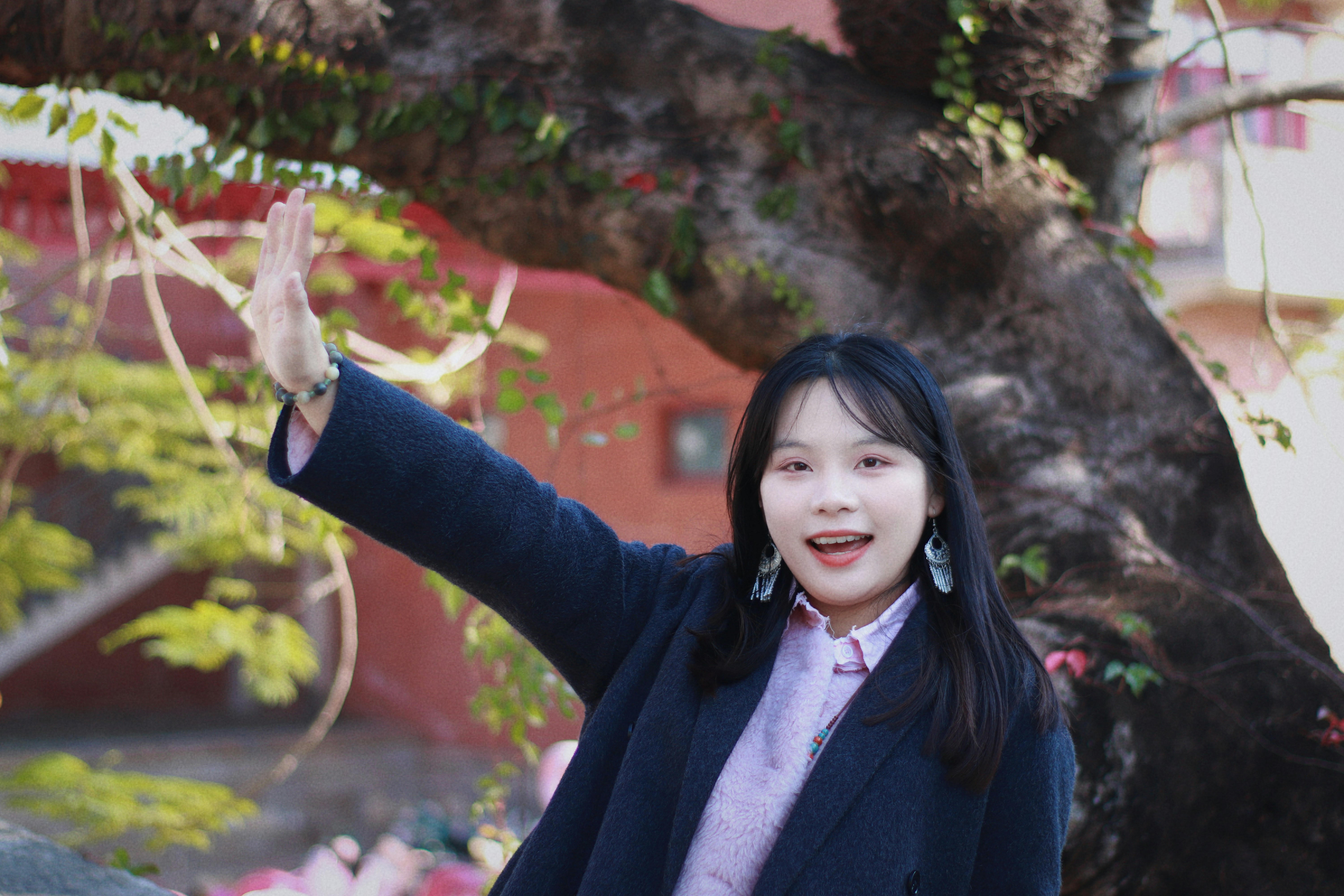 Jeune femme fait signe de la main devant un arbre