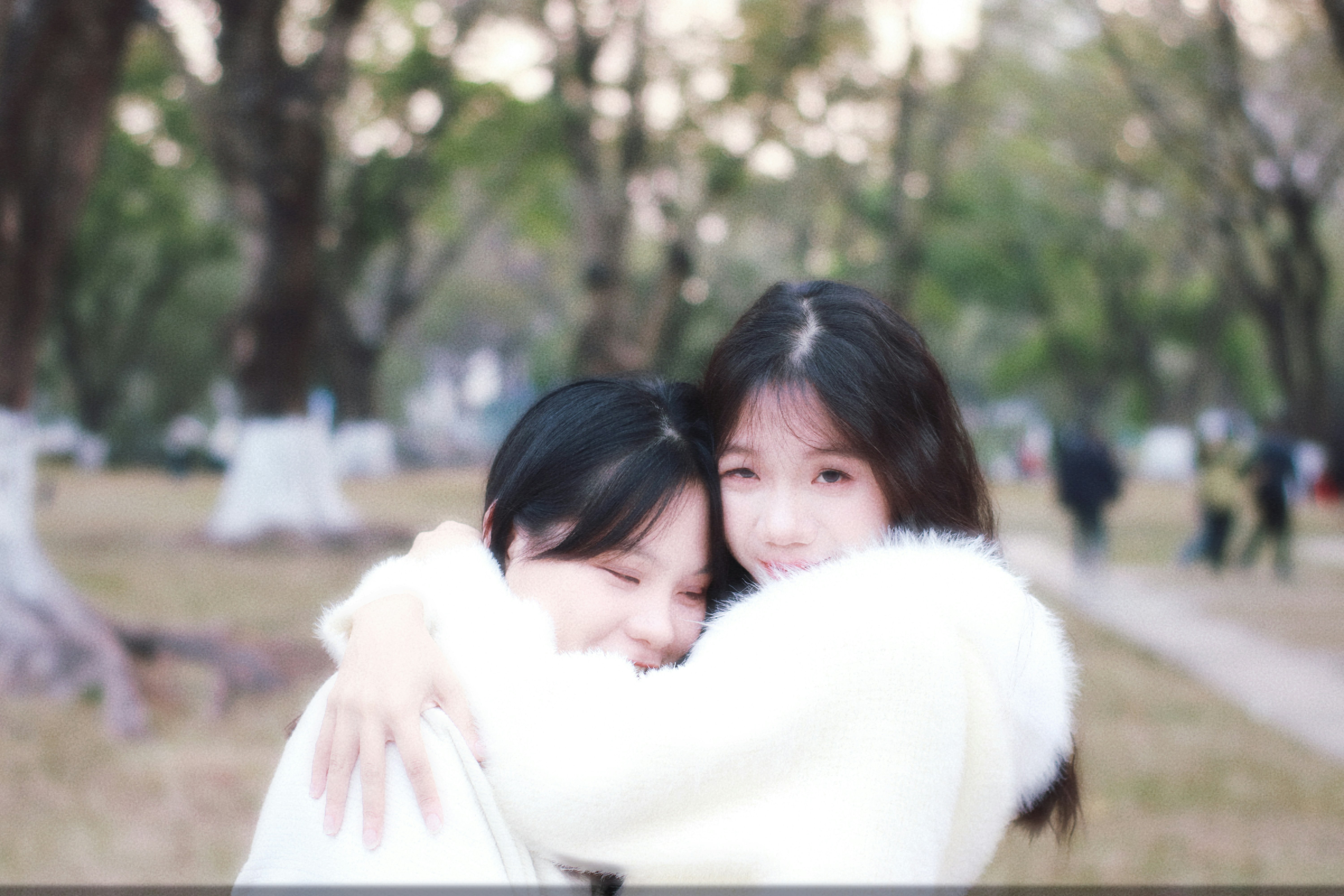 Two young women hugging outdoors in a park.