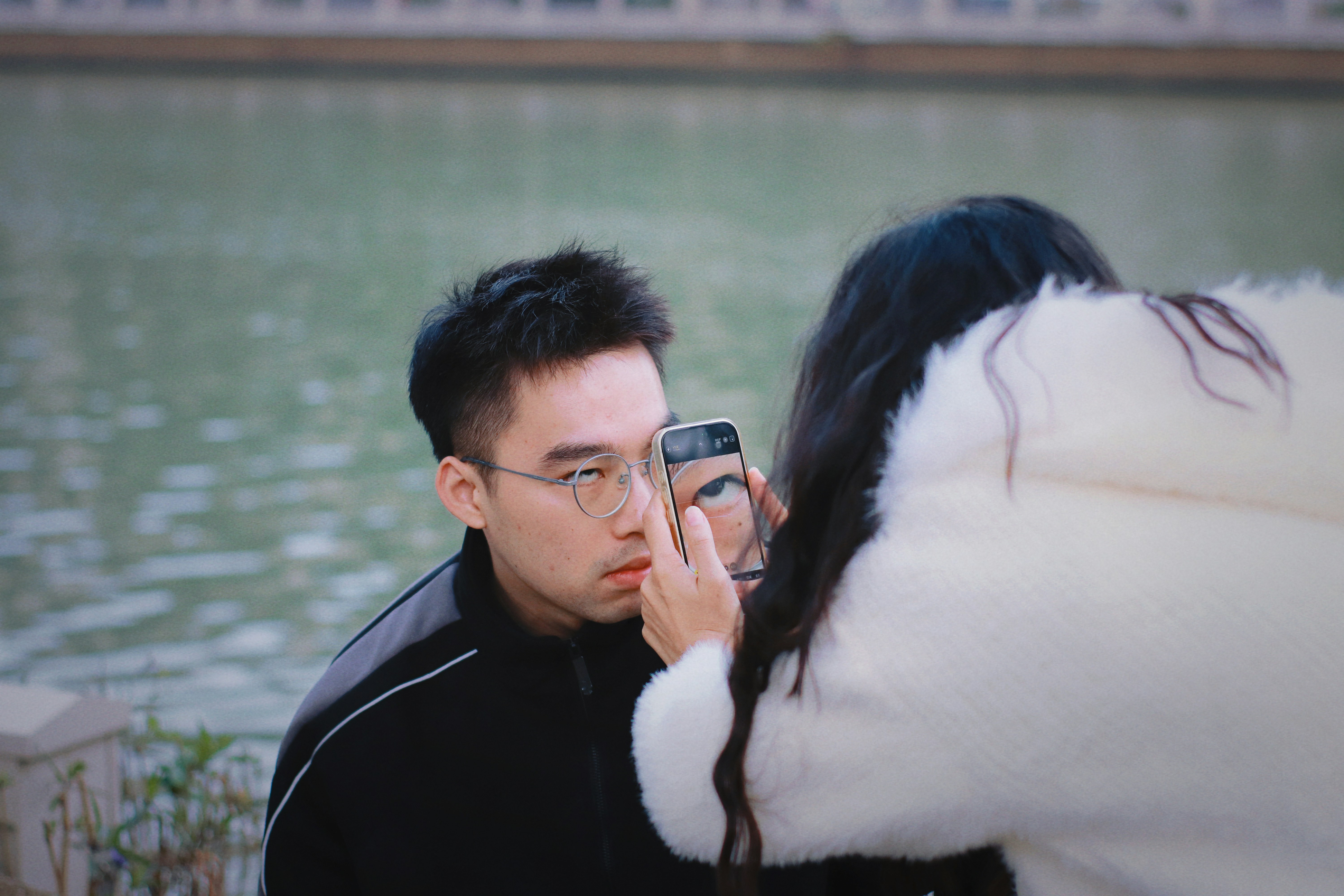 Woman takes a selfie with a man by the water.