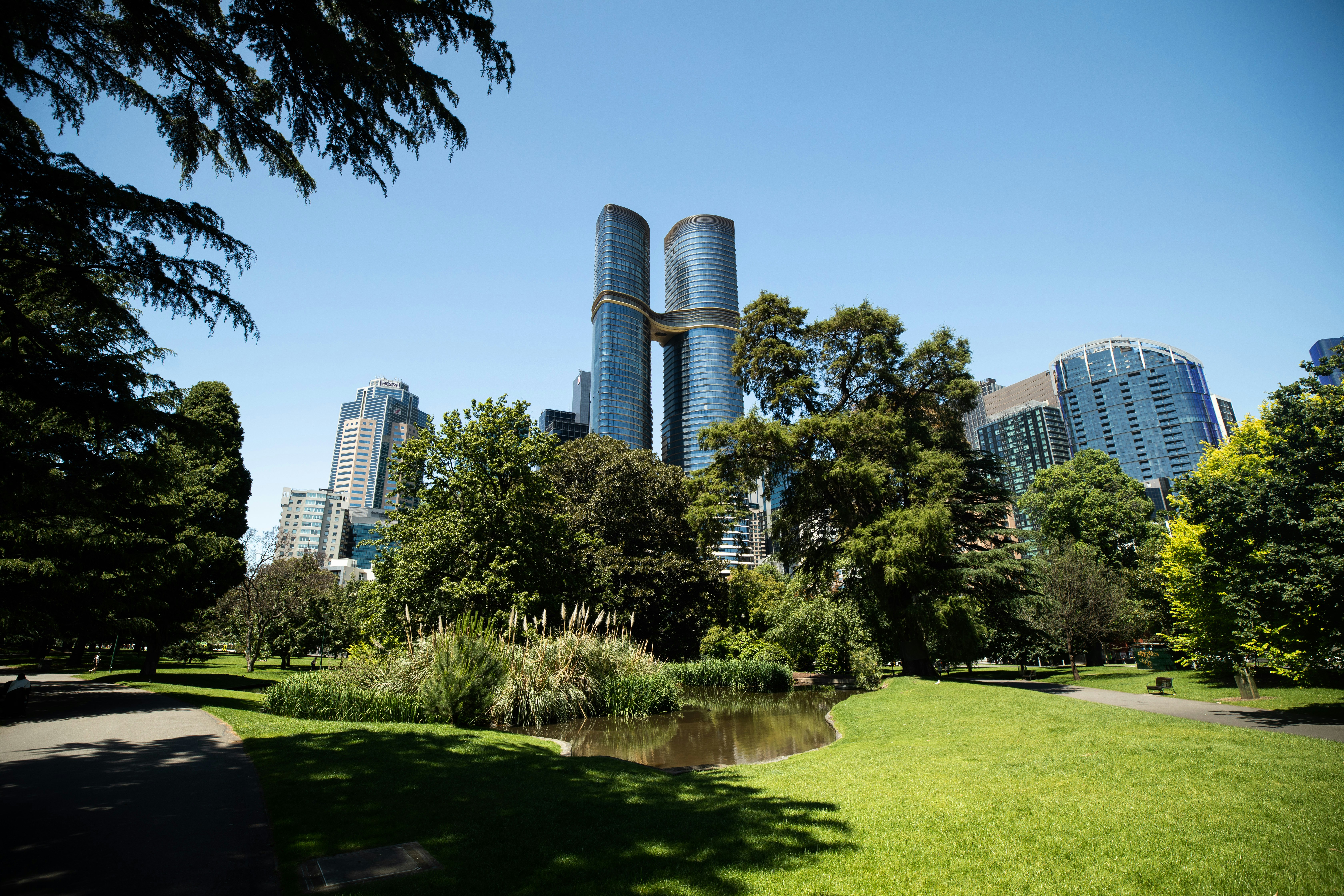 Modern skyscrapers rise behind a lush green park.