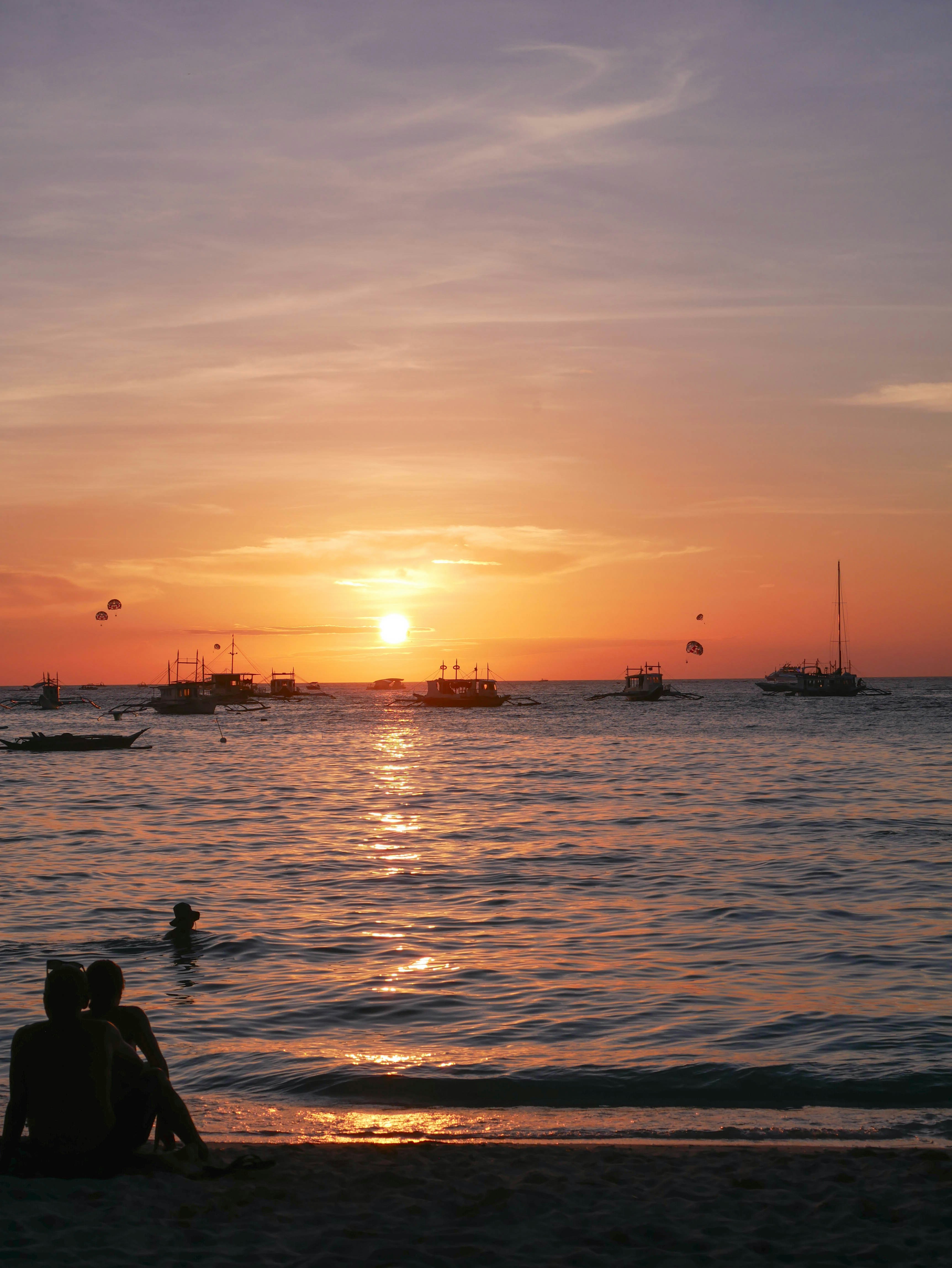 Coppia che guarda un tramonto vibrante sull'oceano con le barche.