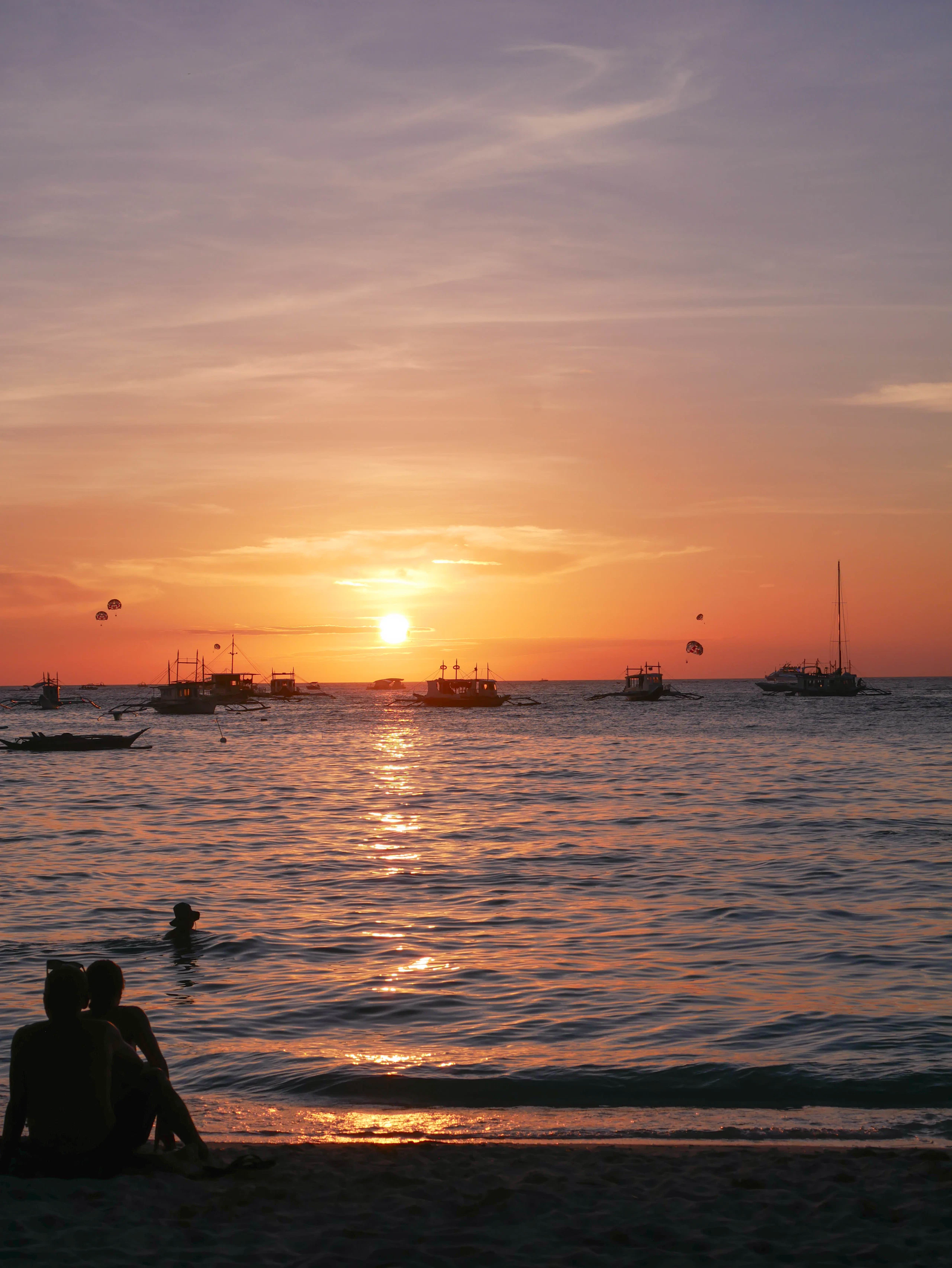 Couple watching a vibrant sunset over the sea with boats