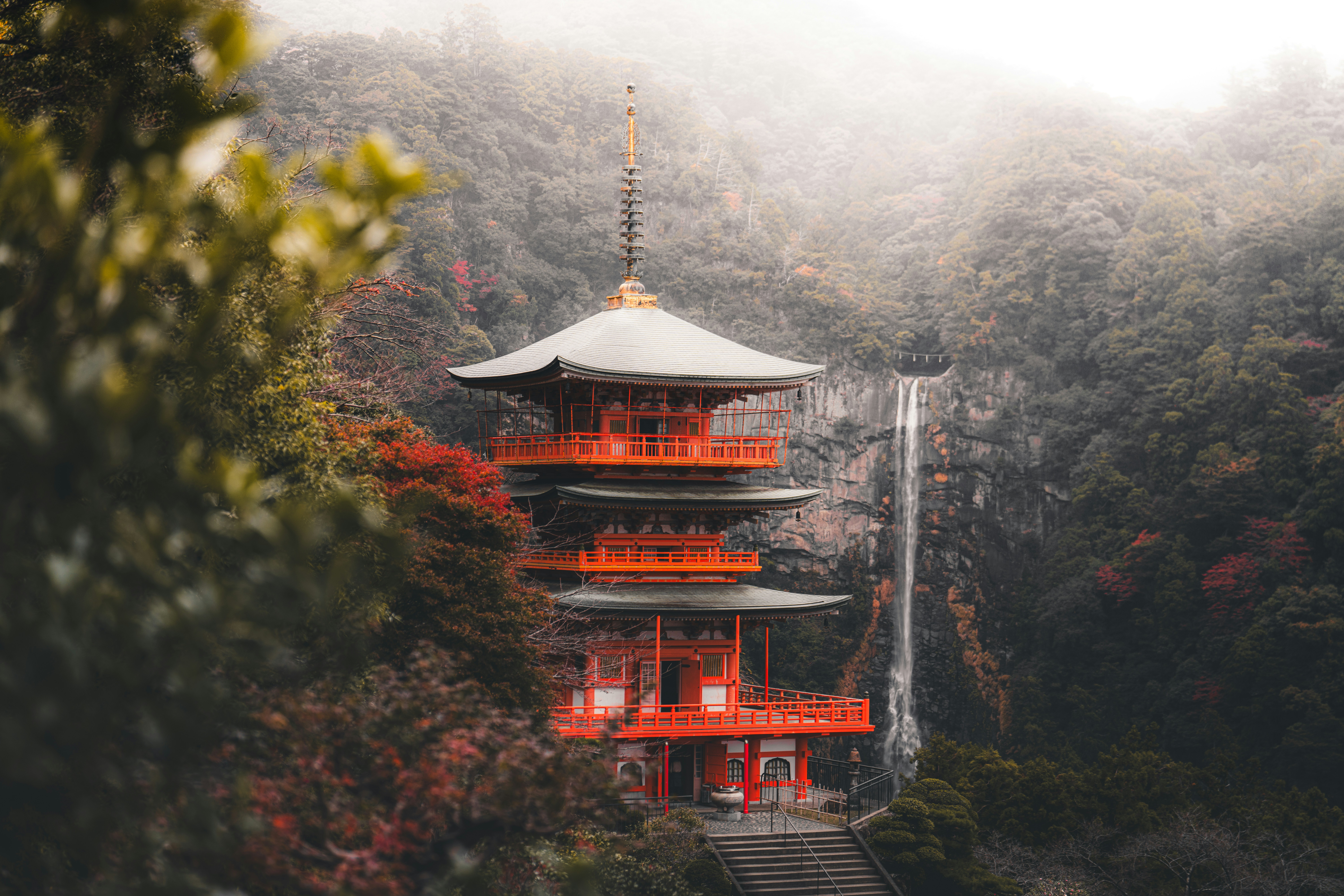 Red pagoda nestled beside a misty waterfall in autumn.