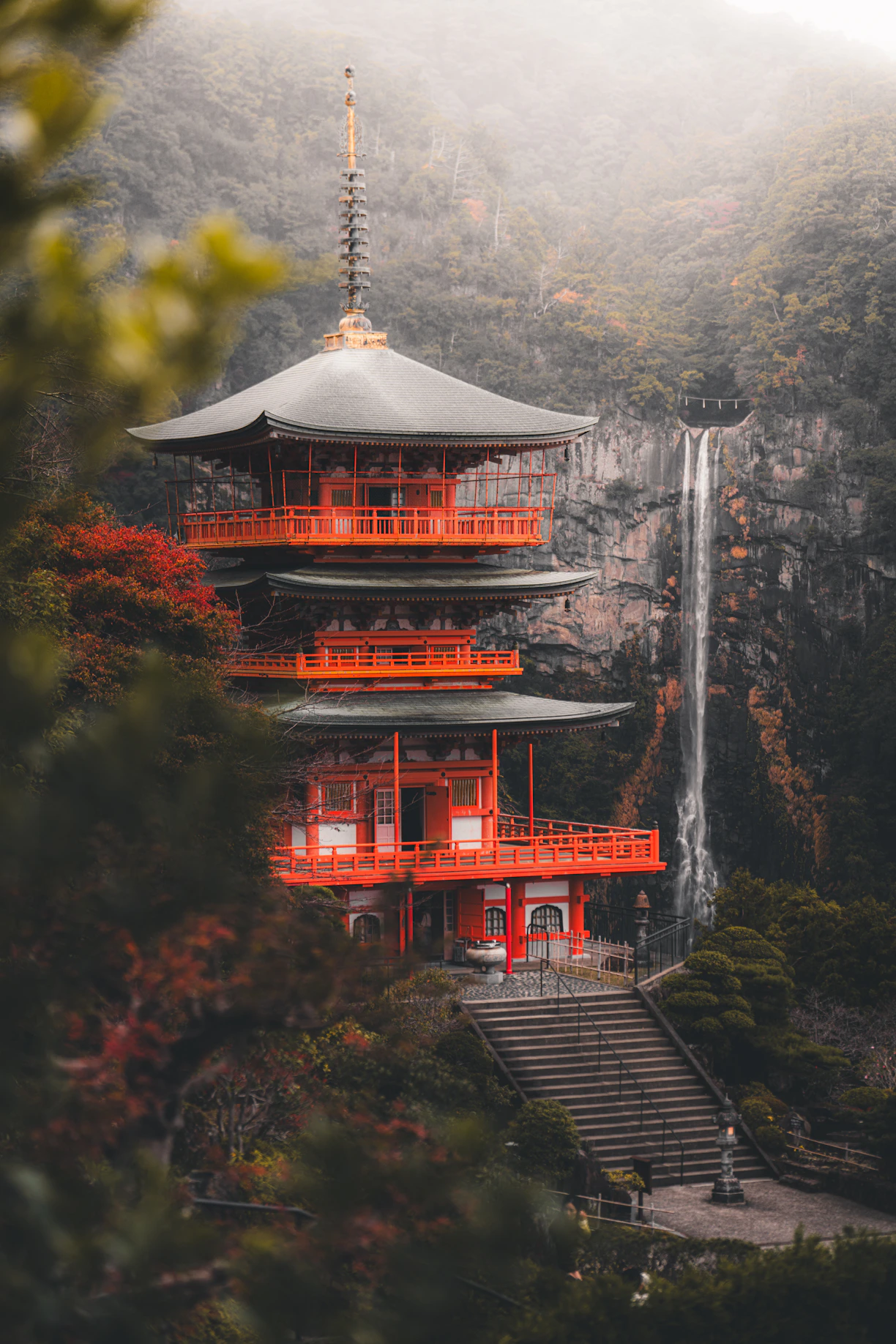 A vibrant red pagoda stands beside a tall waterfall.