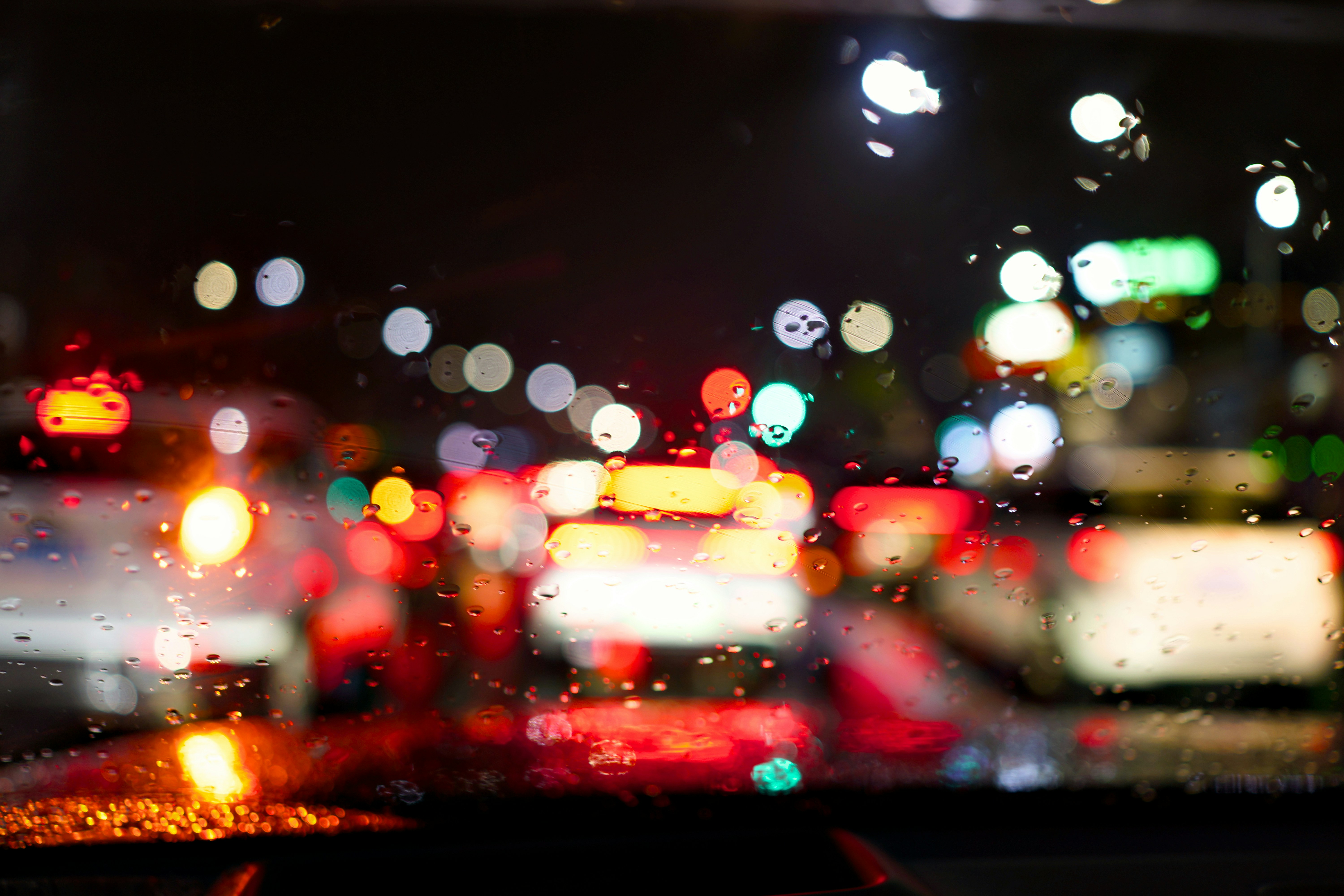 Raindrops on a car windshield at night with bokeh lights.