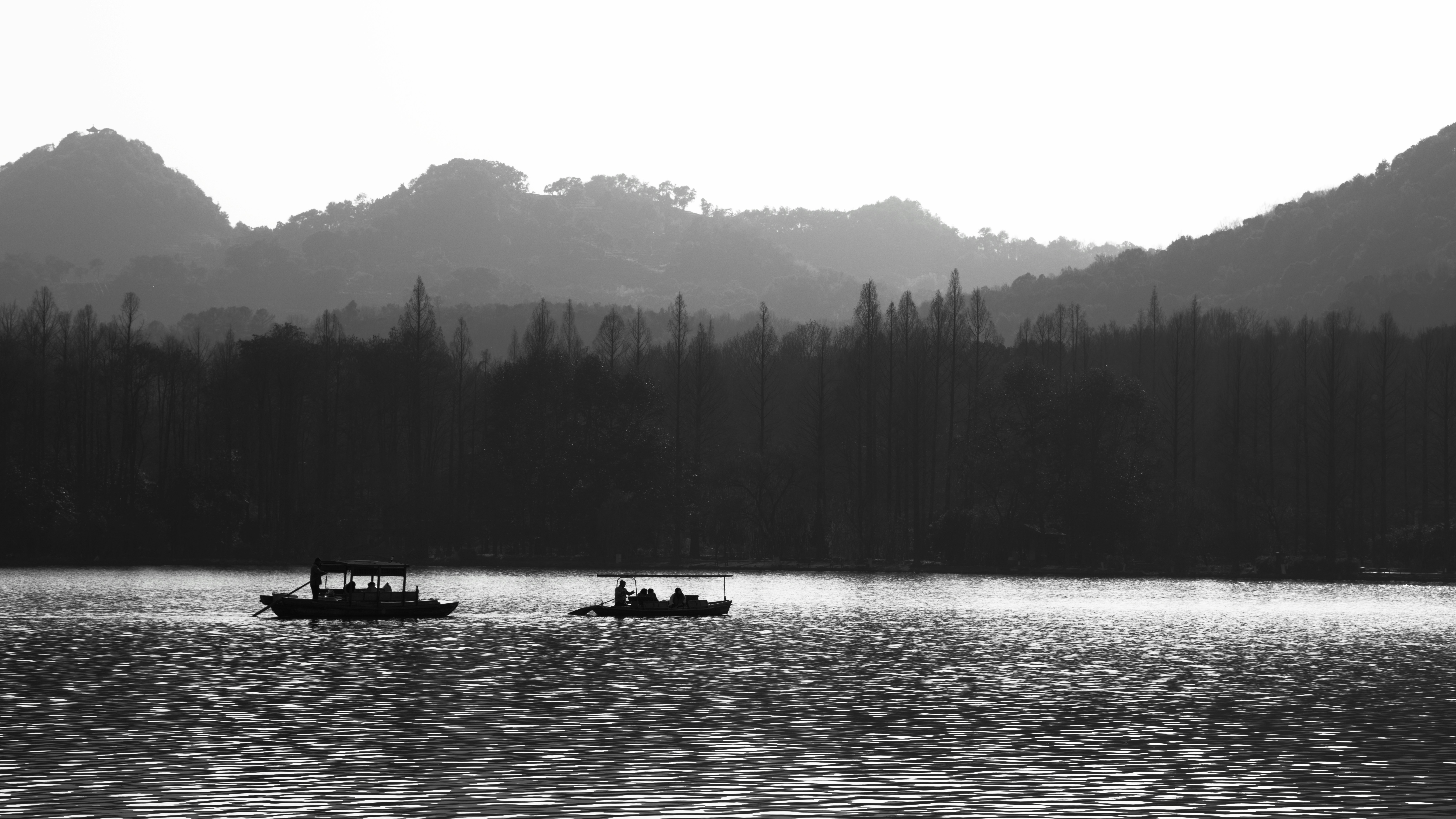 Dos barcos navegan por un lago tranquilo con montañas detrás.