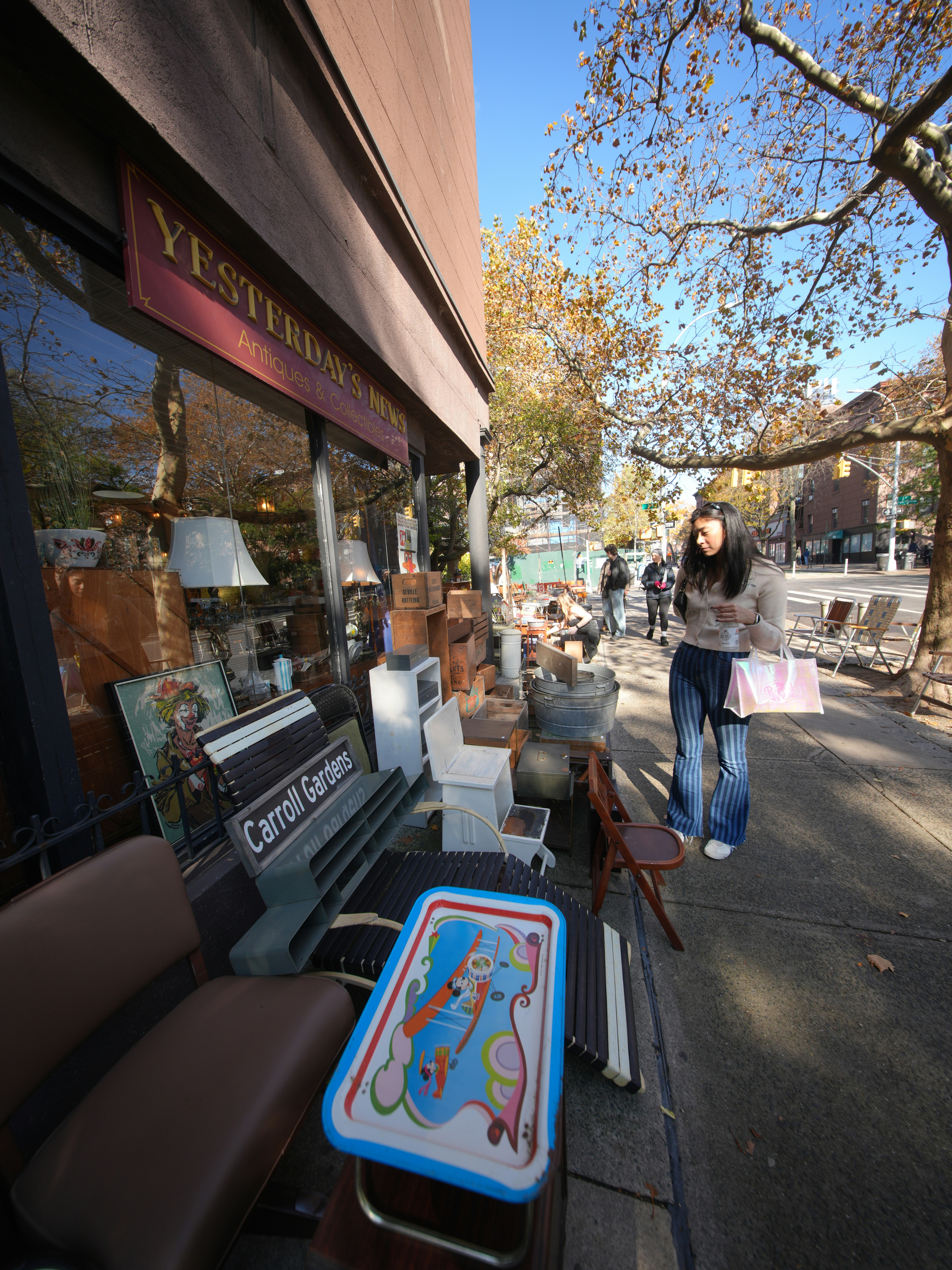 Frau geht an einem Antiquitätengeschäft vorbei, mit Gegenständen draußen