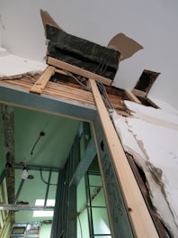 Damaged ceiling and wall with exposed wires and wood framing.