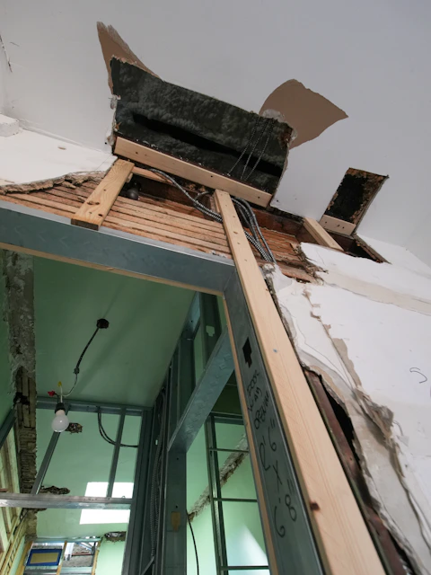 Damaged ceiling and wall with exposed wires and wood framing.
