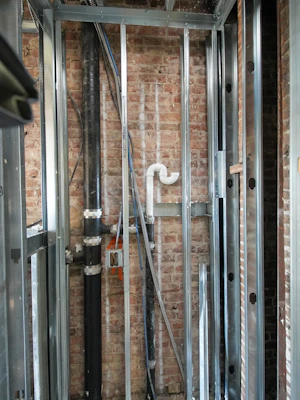Metal studs and plumbing pipes against brick wall.