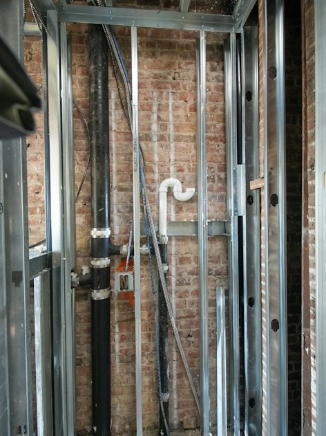 Réseaux d’eau et évacuations en attente devant l’ossature d’une salle d’eau en travaux — Jean Latour BTP