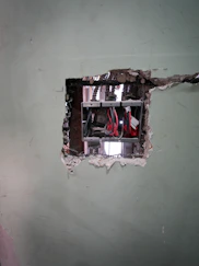 Exposed electrical wiring in a damaged wall opening.