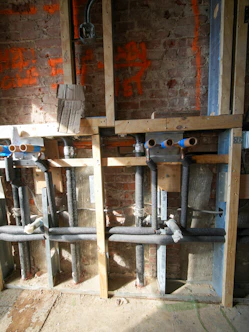 Exposed plumbing pipes and electrical conduit in a wall.