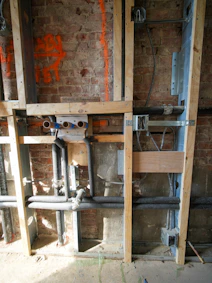 Exposed plumbing and electrical wiring in a brick wall.