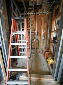 Orange ladder stands in a room under construction.