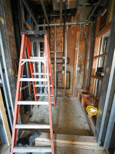 Orange ladder stands in a room under construction.