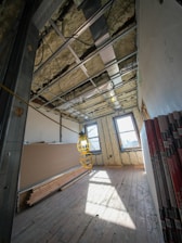 Room under construction with exposed ceiling and drywall sheets.