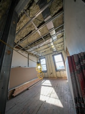 Room under construction with exposed ceiling and drywall sheets.