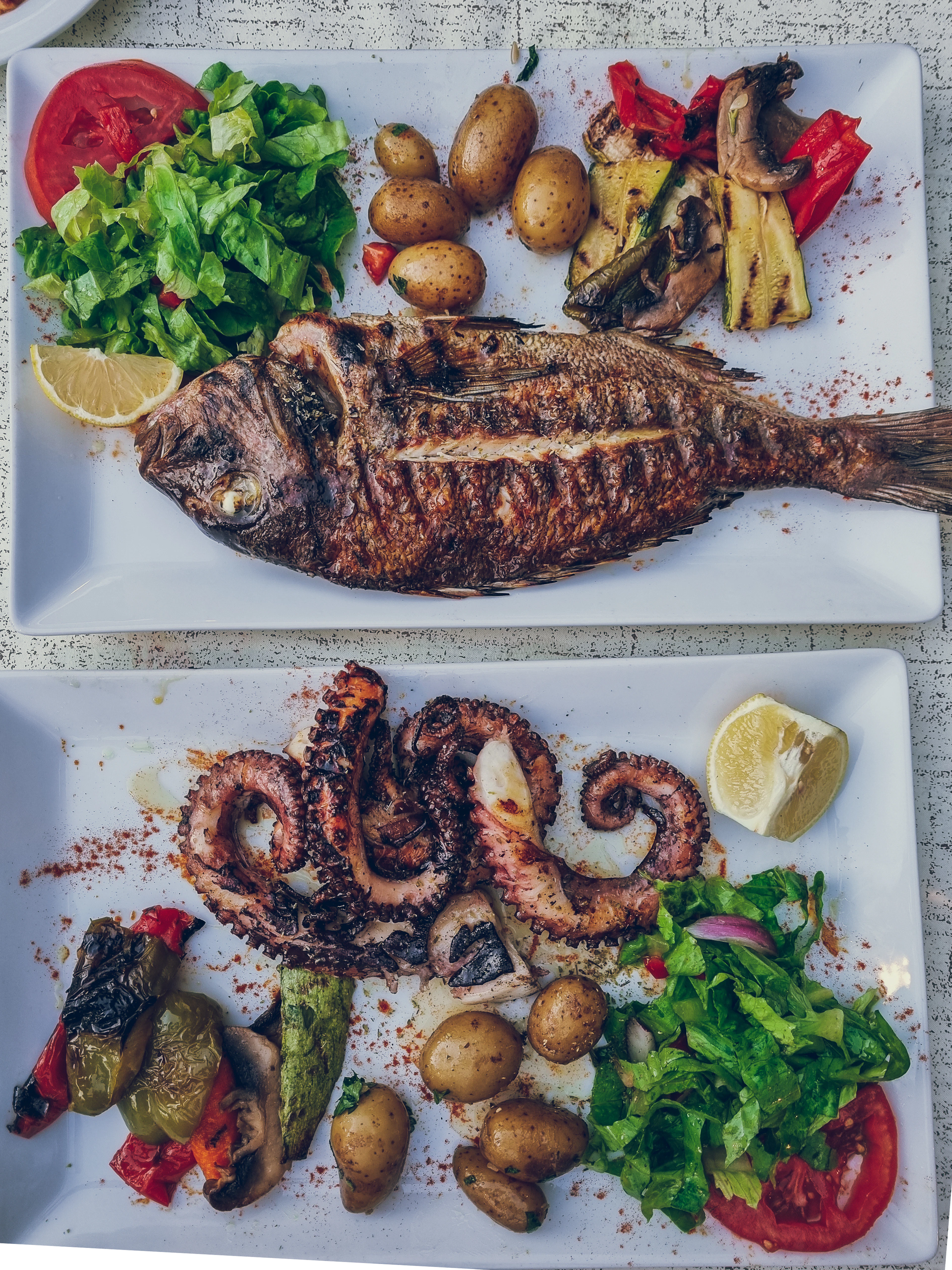Two taverna platters in Greece — a whole grilled fish with salad, boiled potatoes and grilled peppers, and a plate of chargrilled octopus tentacles dusted with paprika and served with lemon