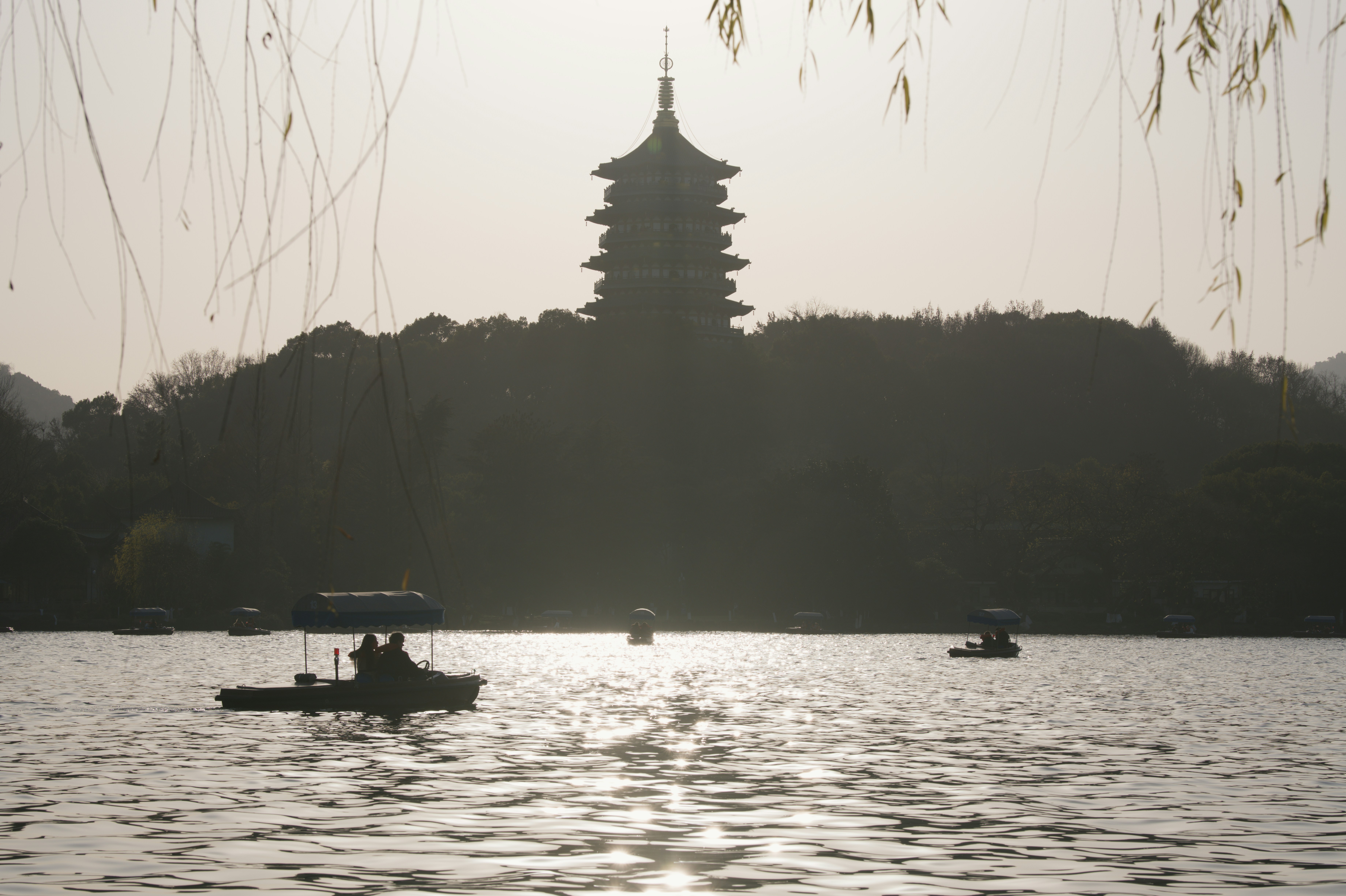 Silueta de pagoda sobre un lago con barcas de remos