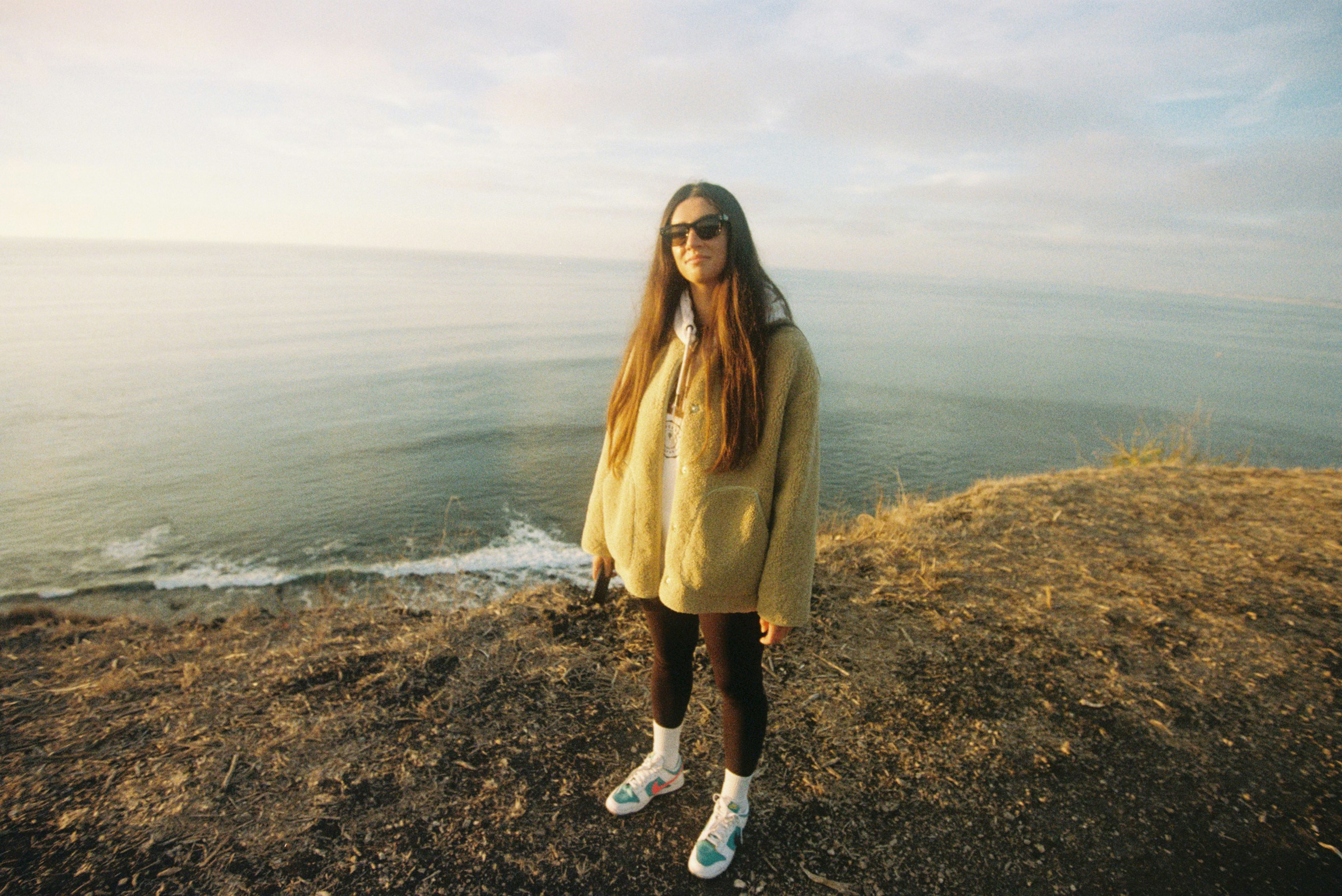 Joven de pie en un acantilado con vistas al océano.
